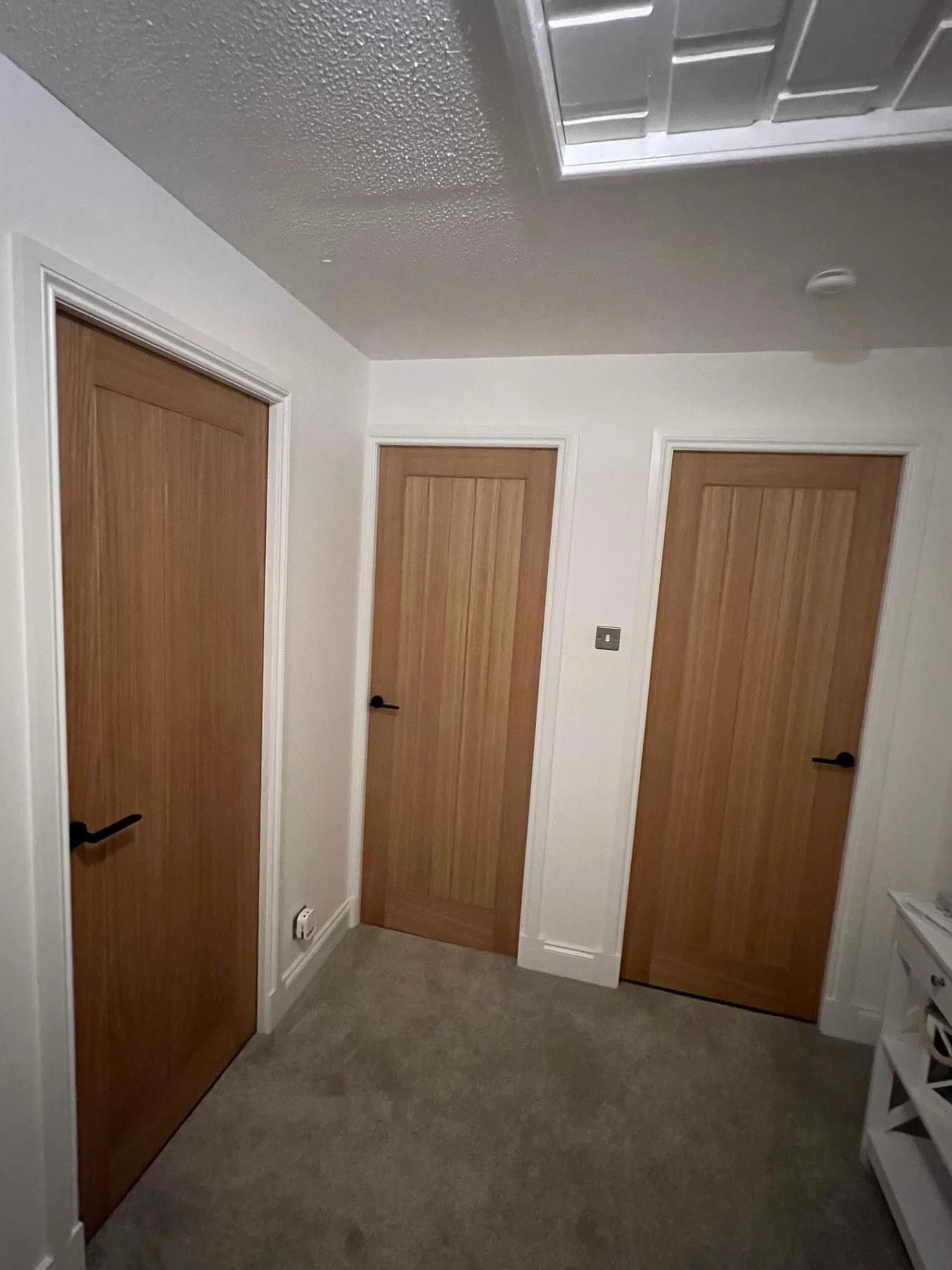 A room with three closed wooden doors, white walls, a light-colored carpeted floor, and a white ceiling with a ceiling vent.
