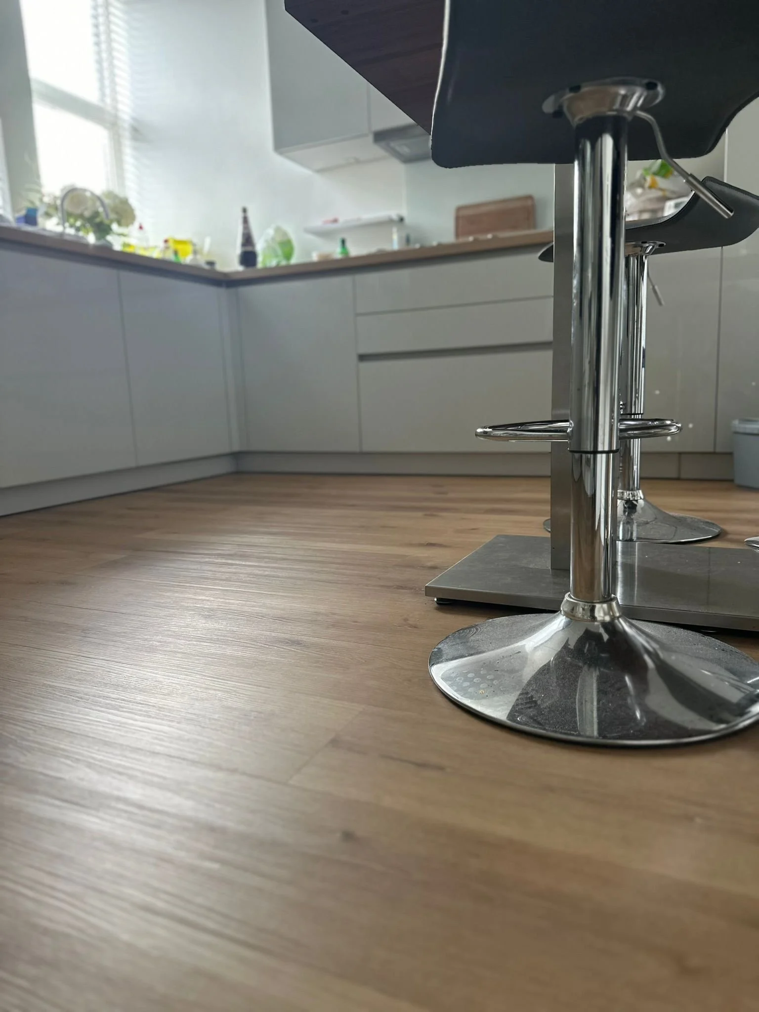 Close-up of a modern kitchen with wooden flooring, white cabinets, a granite countertop, and metal barstools.