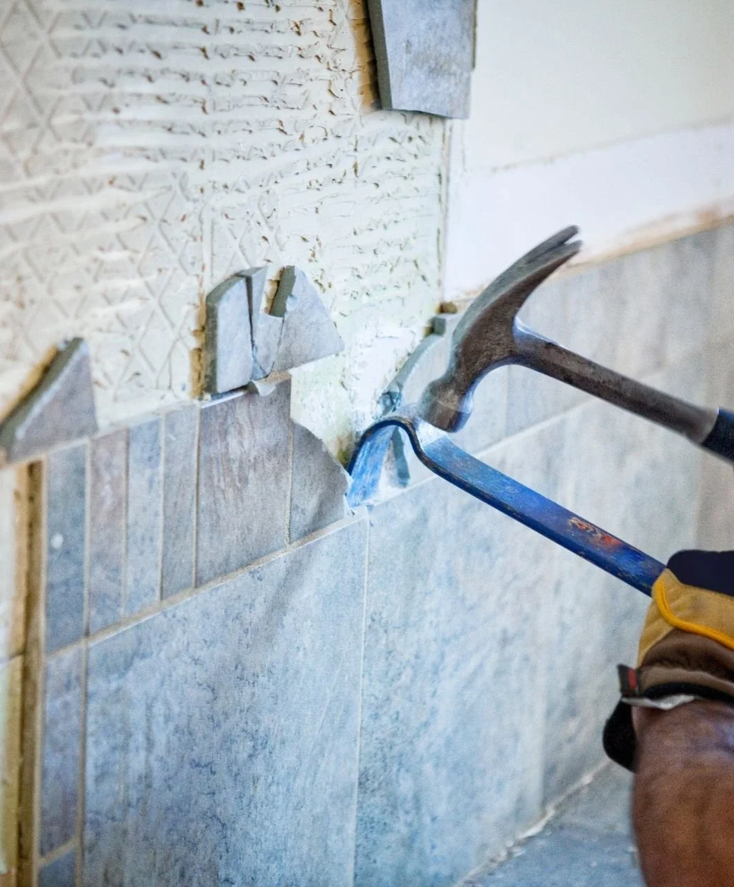 A worker is installing or removing tiles from a wall using a hammer and chisel.