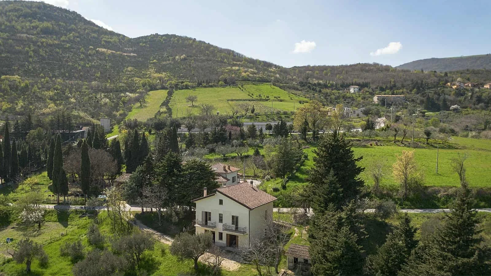 Scenic view of a rural landscape with hills, trees, houses, and green fields on a sunny day.