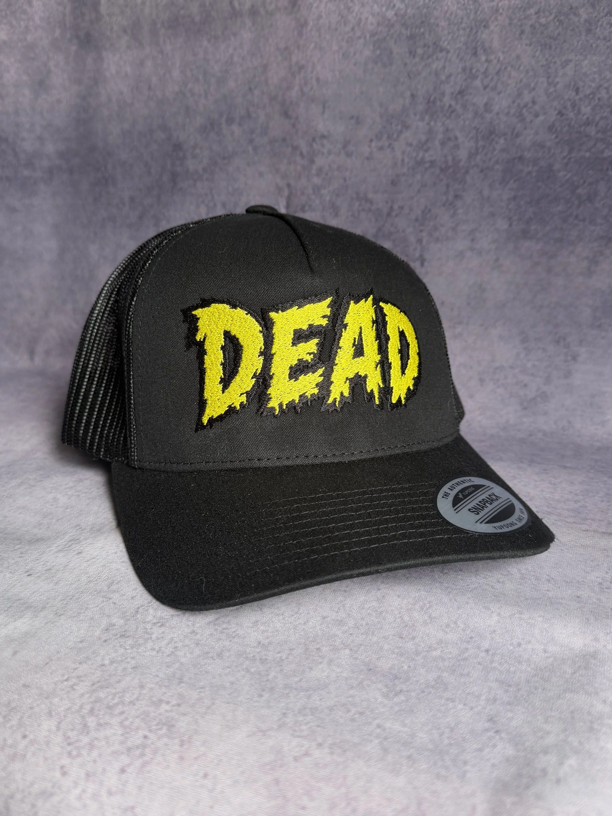 Black Yupoong trucker cap with yellow DEAD horror lettering