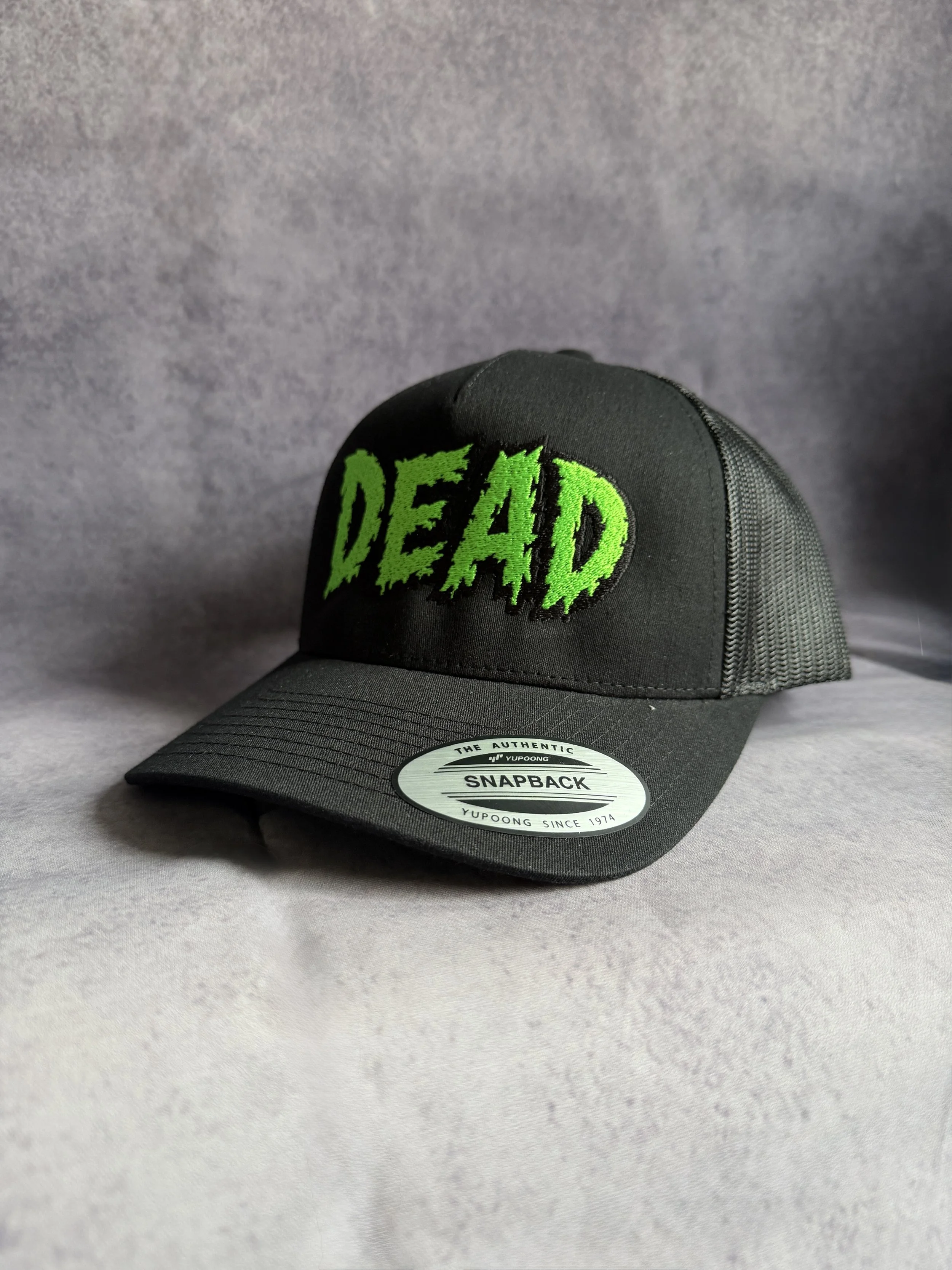 Green DEAD snapback cap angled to show the Yupoong visor and mesh back