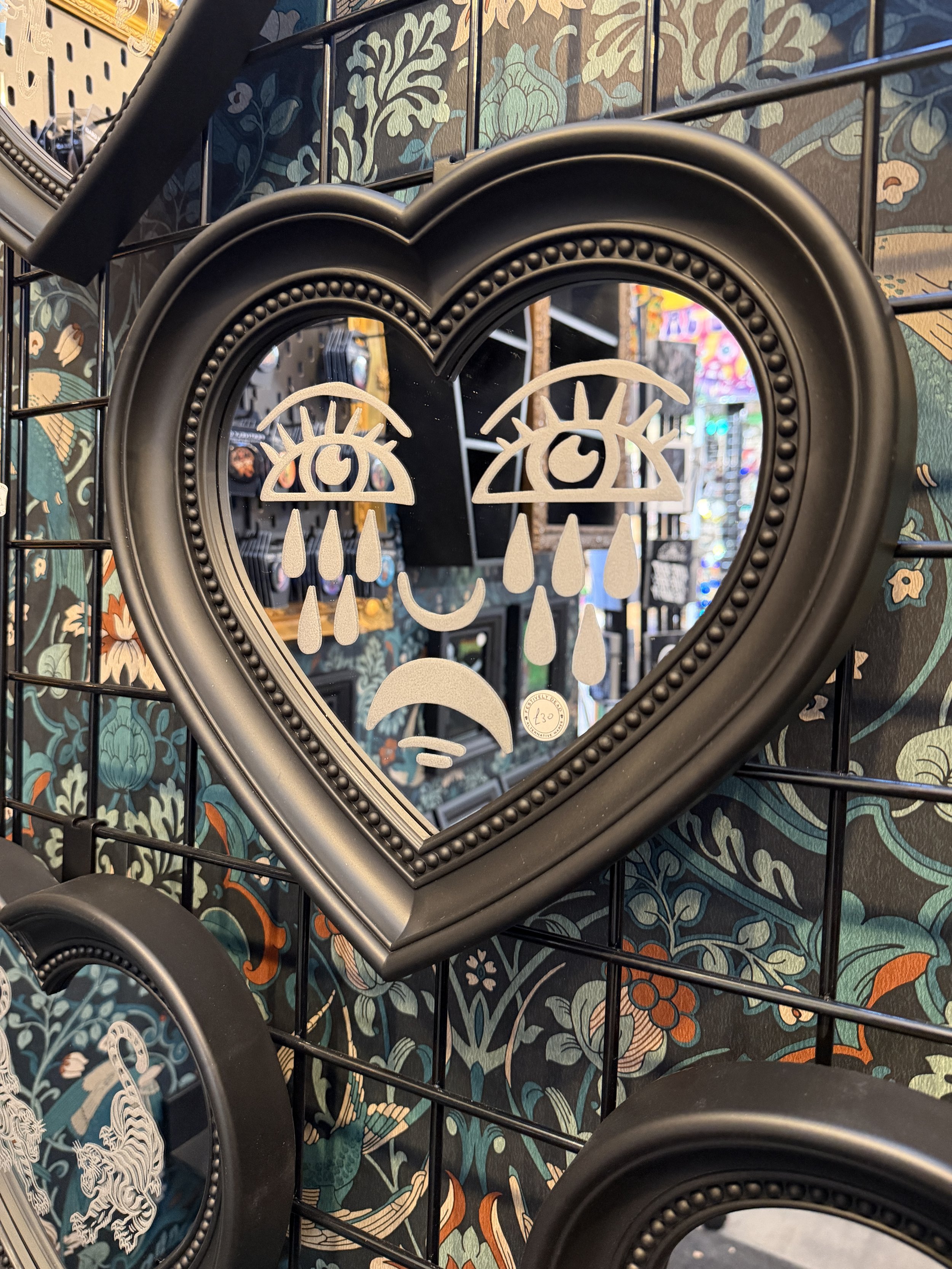 Evil eye heart mirror hung on a dark patterned wall