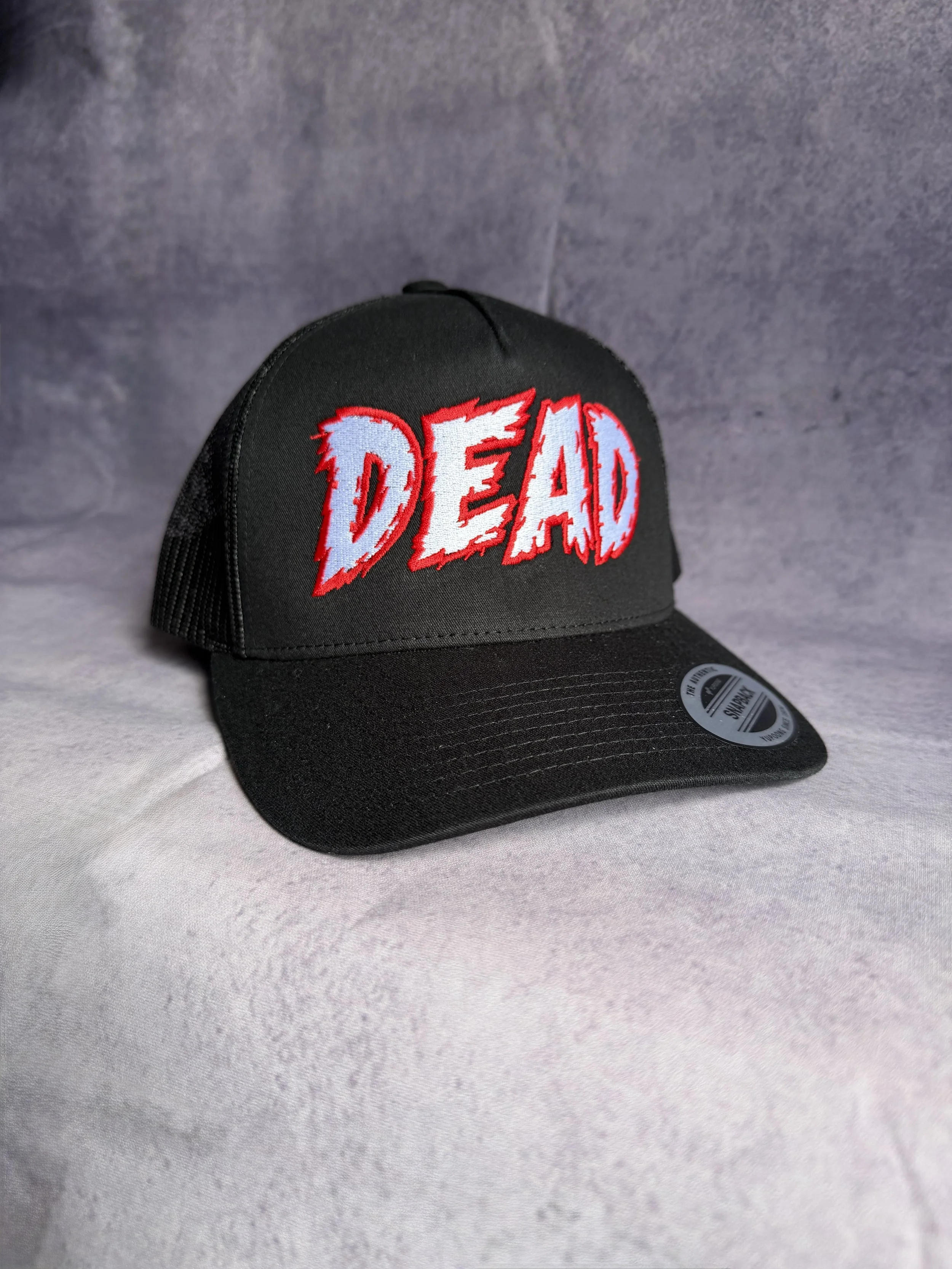 Black trucker cap with white and red DEAD horror lettering embroidered on the front