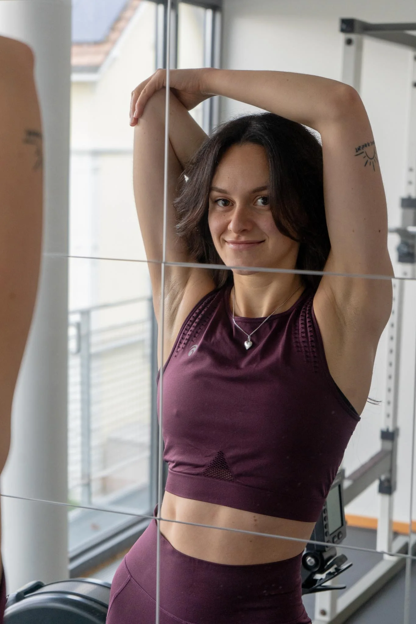 Jeune femme faisant de l'exercice dans une salle de sport, portant une tenue de sport violet et un collier avec un cœur.