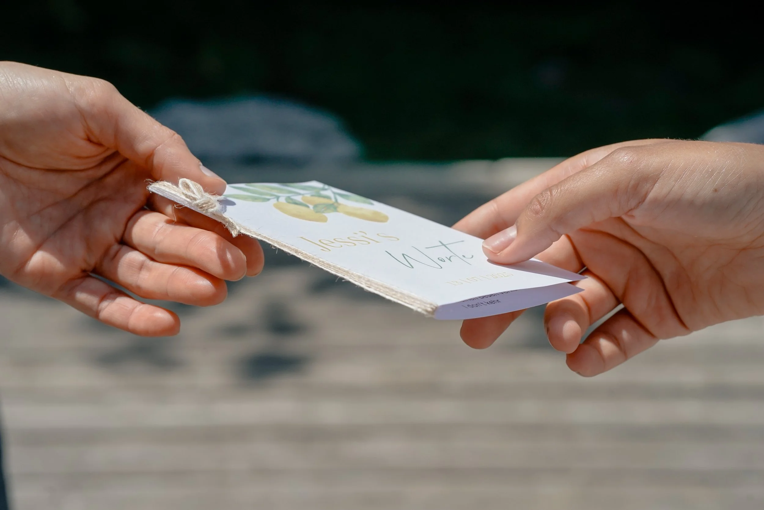 Zwei Hände übergeben sich ein kleines, handgemachtes Buch, das Trauversprechen, mit einer Illustration von Zitronen.