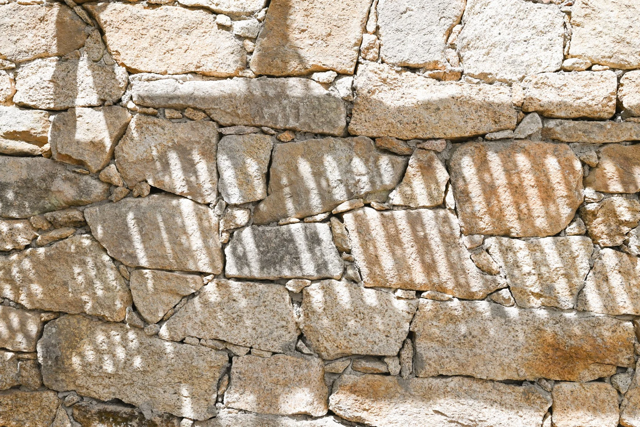 Muro de piedras con sombra que forma líneas diagonales en ellas.