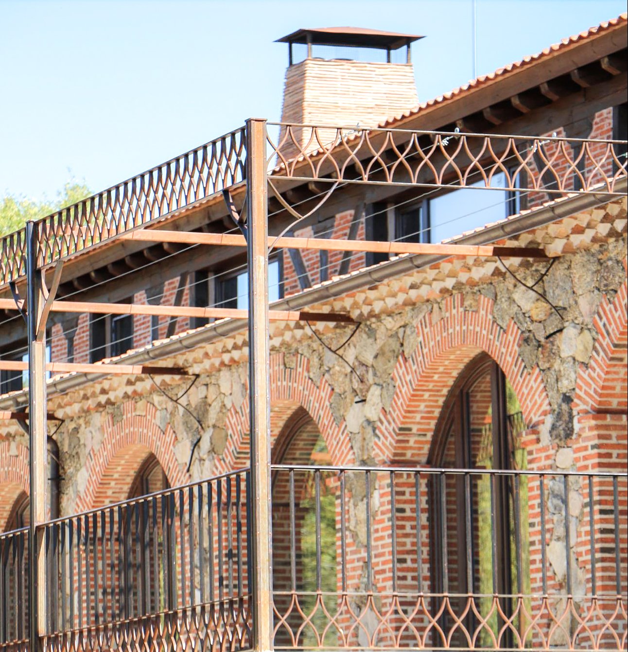 Construcción de casa con estructuras de metal con rejas y arcos de ladrillo y piedra, ventanas con barandas y chimenea en el techo.