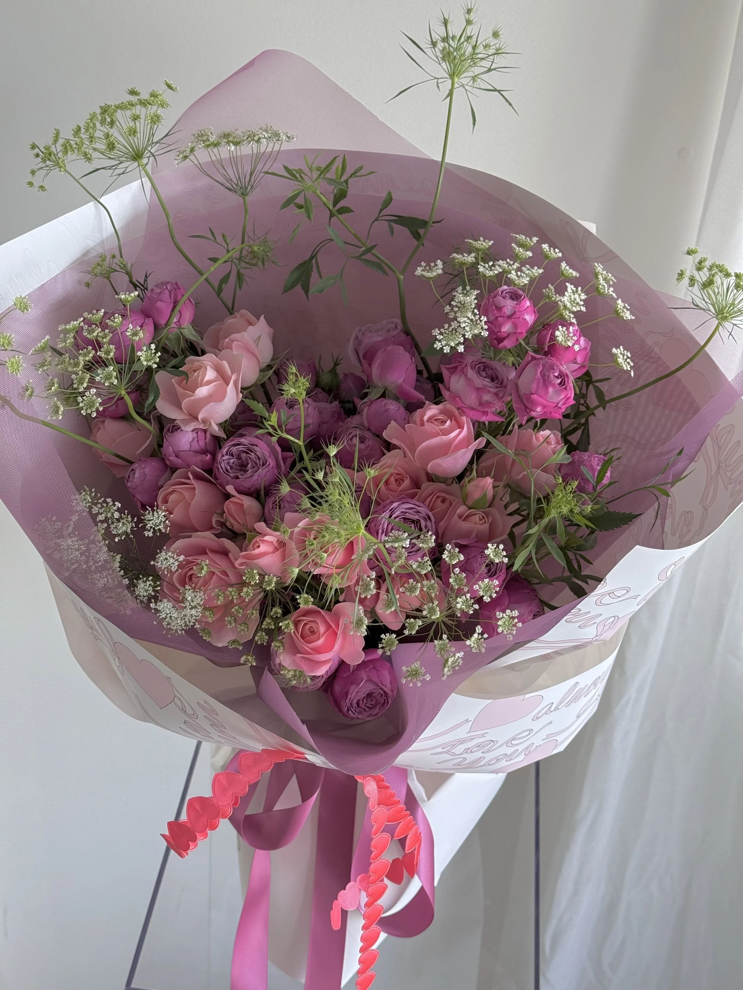 Pink and purple flower bouquet wrapped in pink paper with pink ribbons.