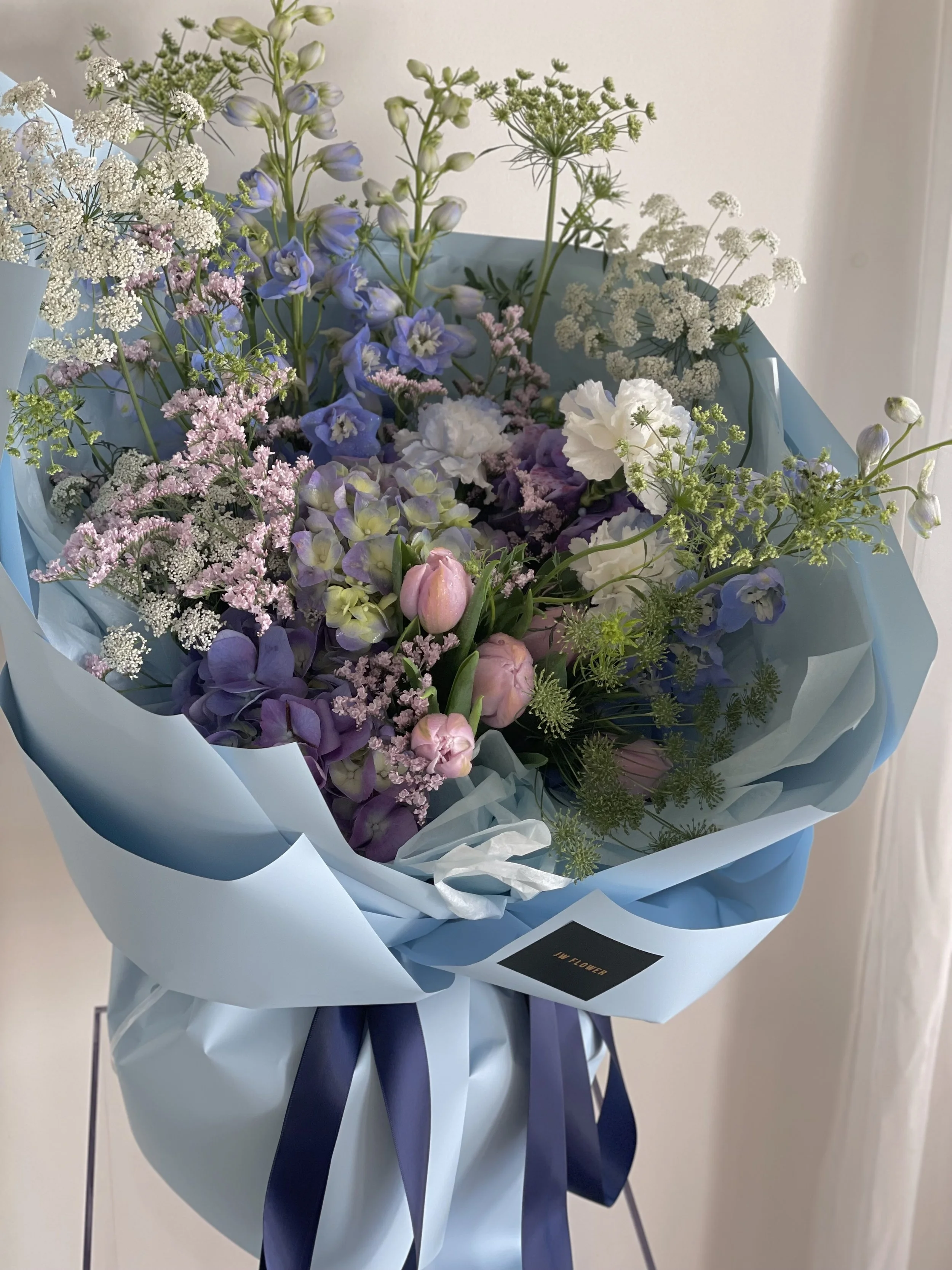 A bouquet of mixed flowers wrapped in blue paper with purple and white ribbons.