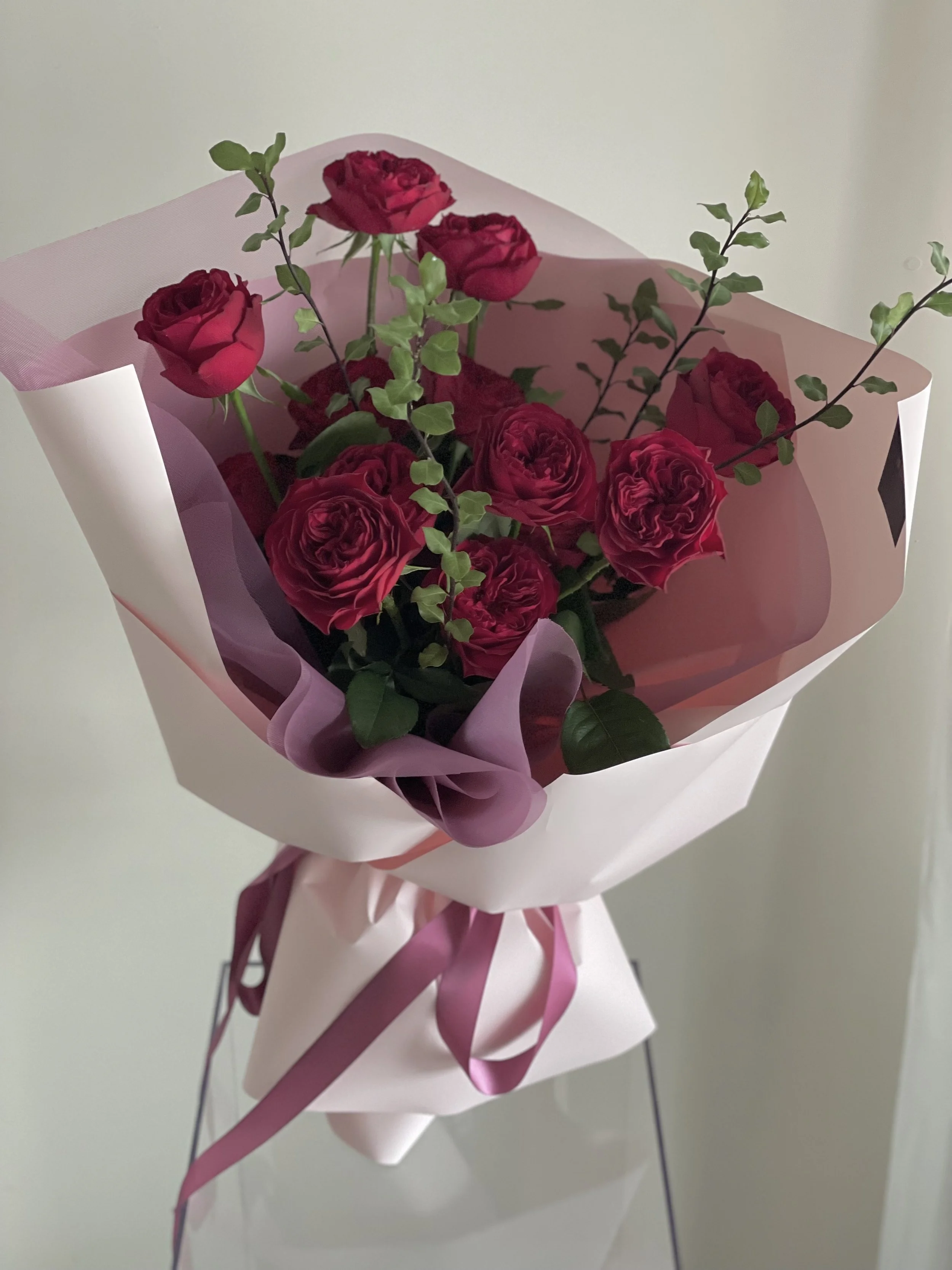 Red roses bouquet wrapped in pink and white paper with purple ribbons.