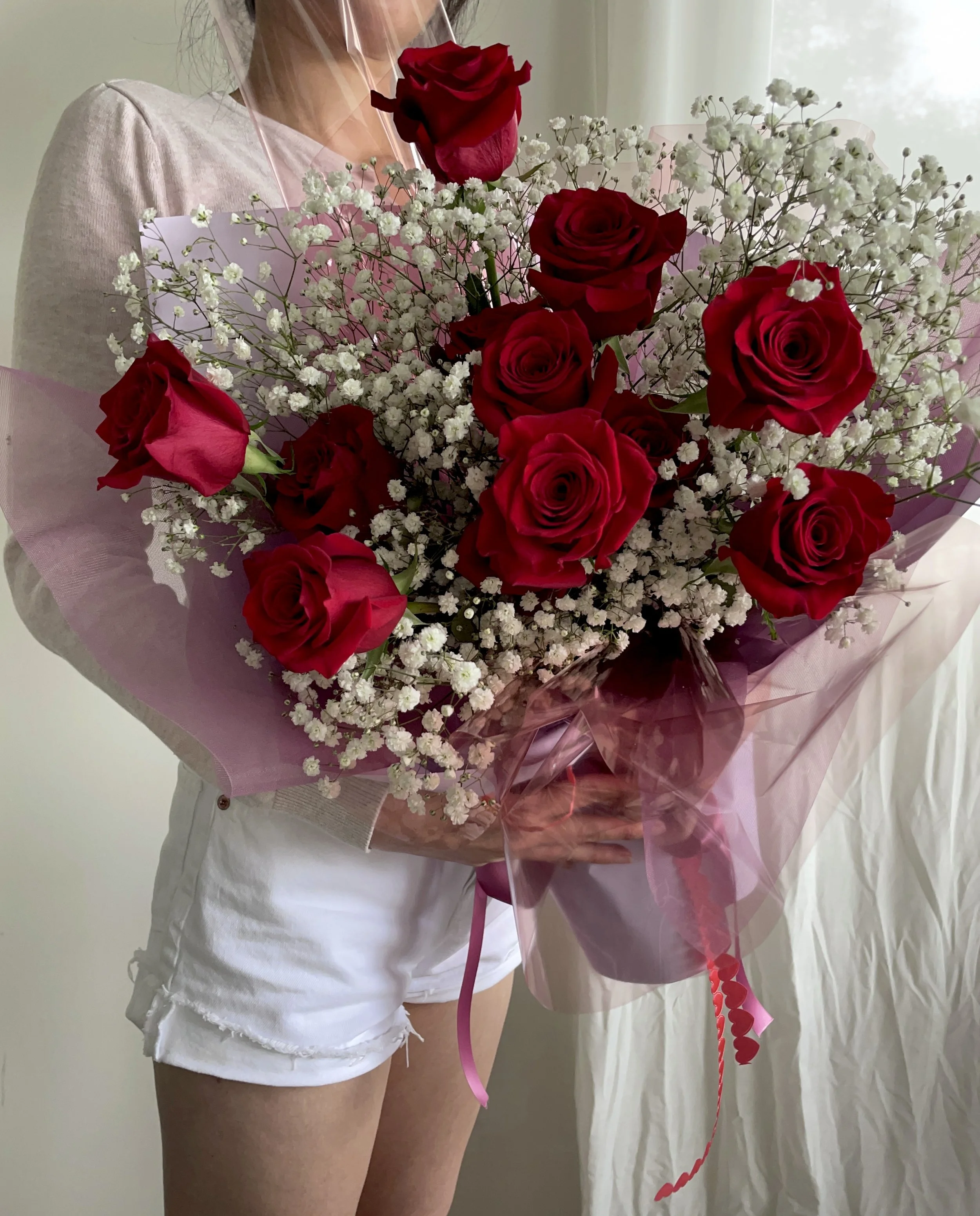 Person holding a large bouquet of red roses and white baby’s breath flowers wrapped in pink and clear cellophane.