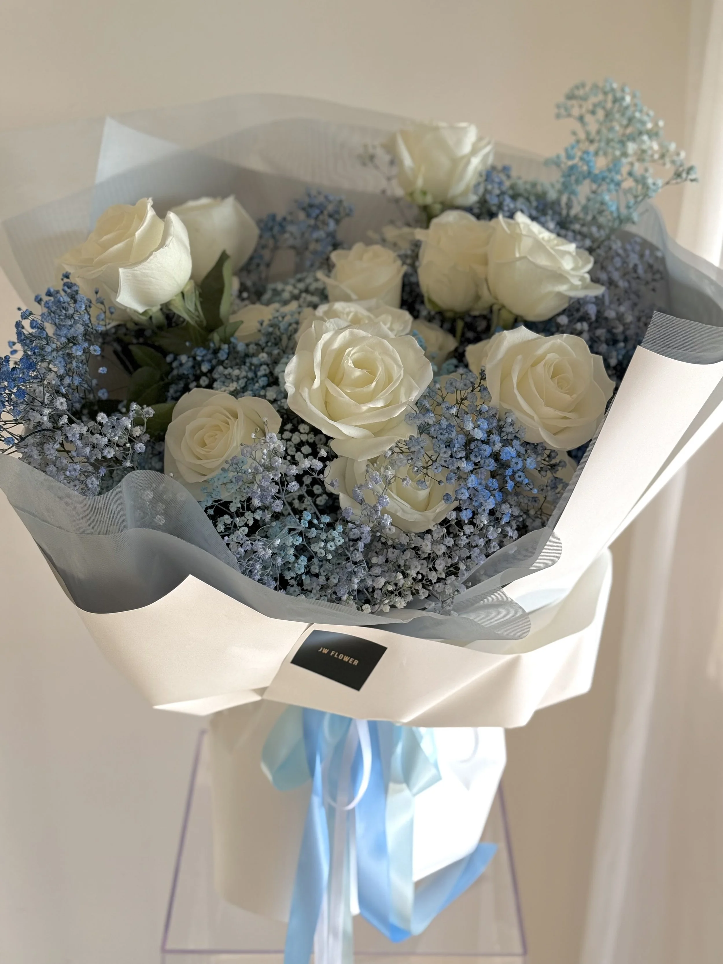 A bouquet of white roses and blue baby's breath wrapped in white paper and tied with a light blue ribbon.
