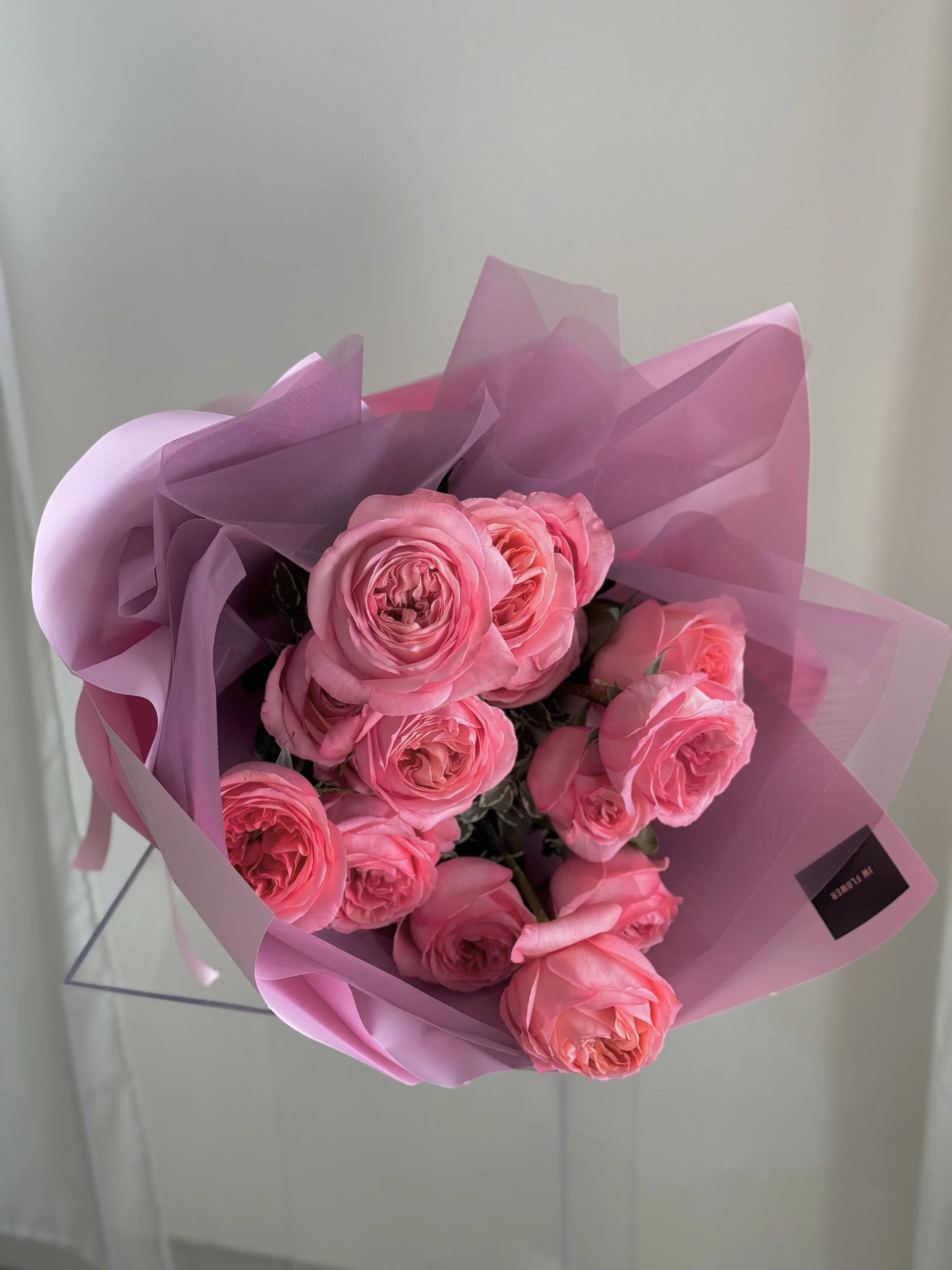 A bouquet of pink roses wrapped in pink and purple tissue paper.