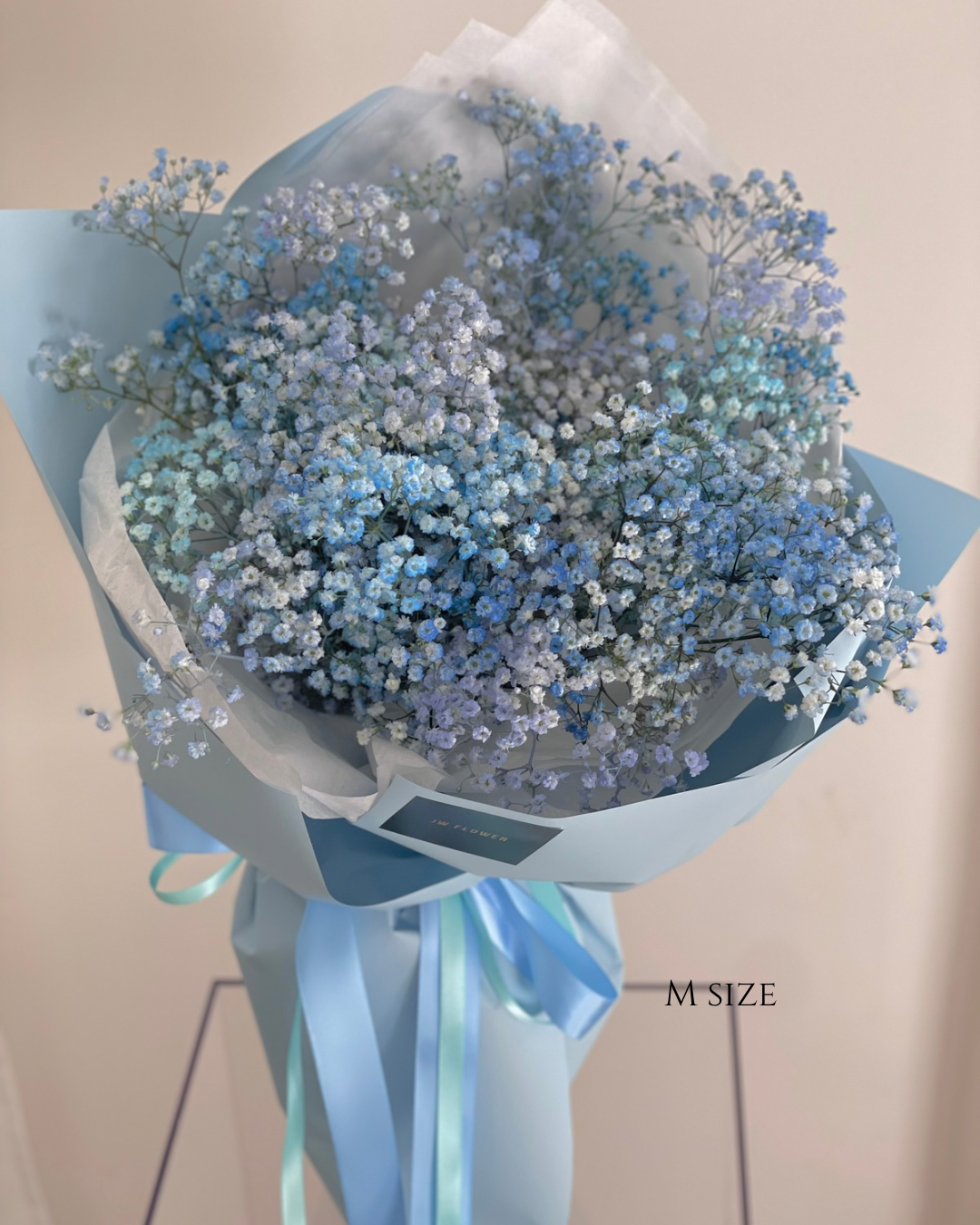 A large bouquet of blue and white baby's breath flowers wrapped in light blue paper with a blue ribbon, labeled 'M SIZE'.