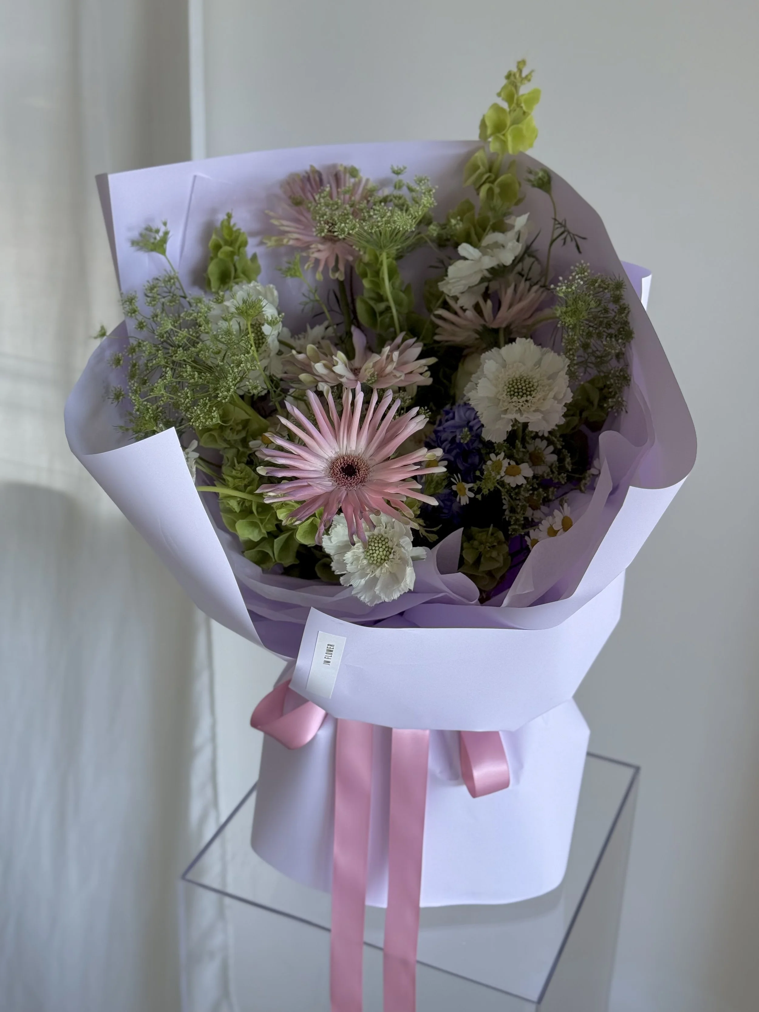 Pink, white, and purple mixed flower bouquet wrapped in white and lavender paper with pink ribbons.