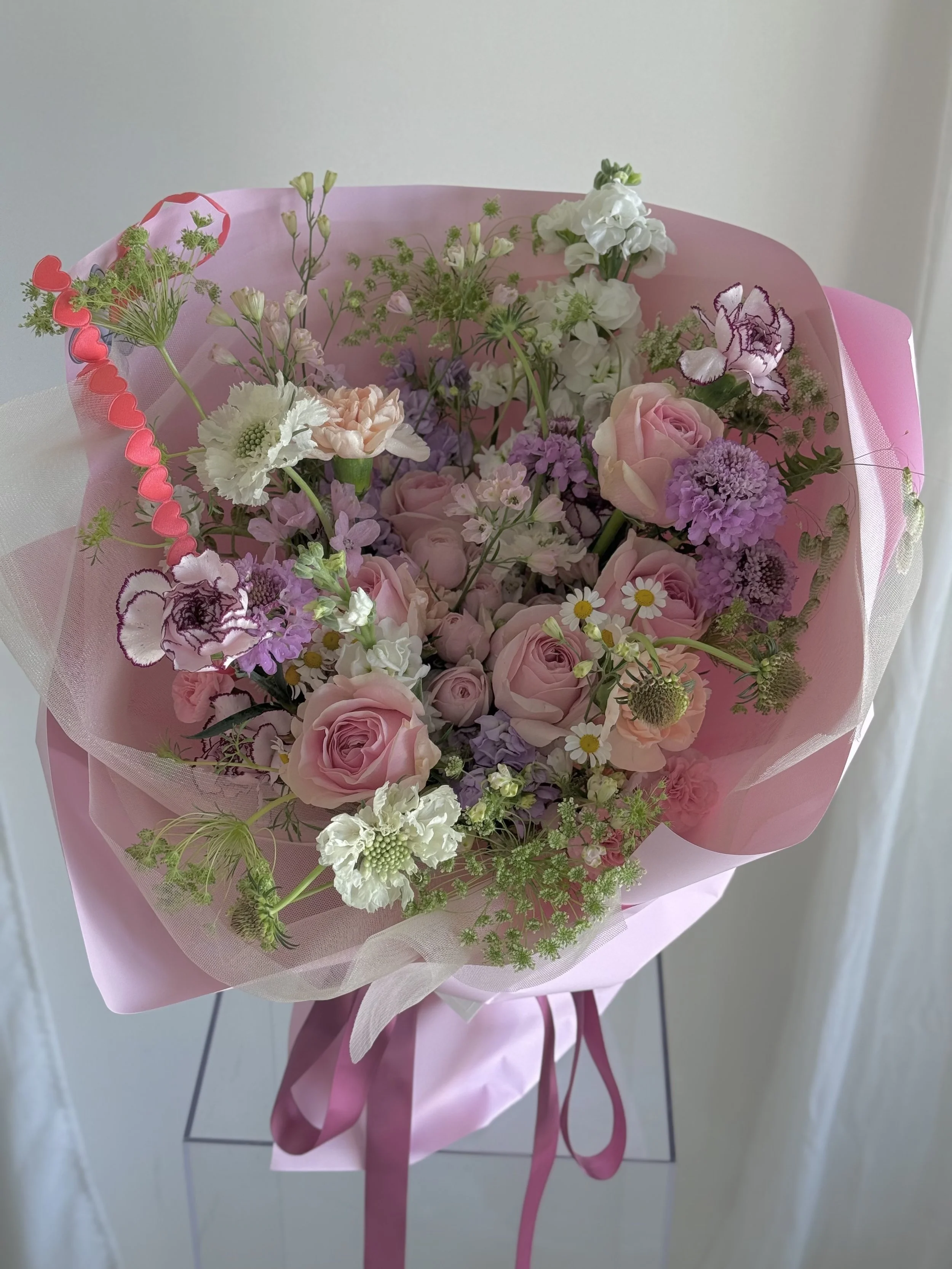 Pink floral bouquet with roses, daisies, and other flowers wrapped in pink paper and ribbon.
