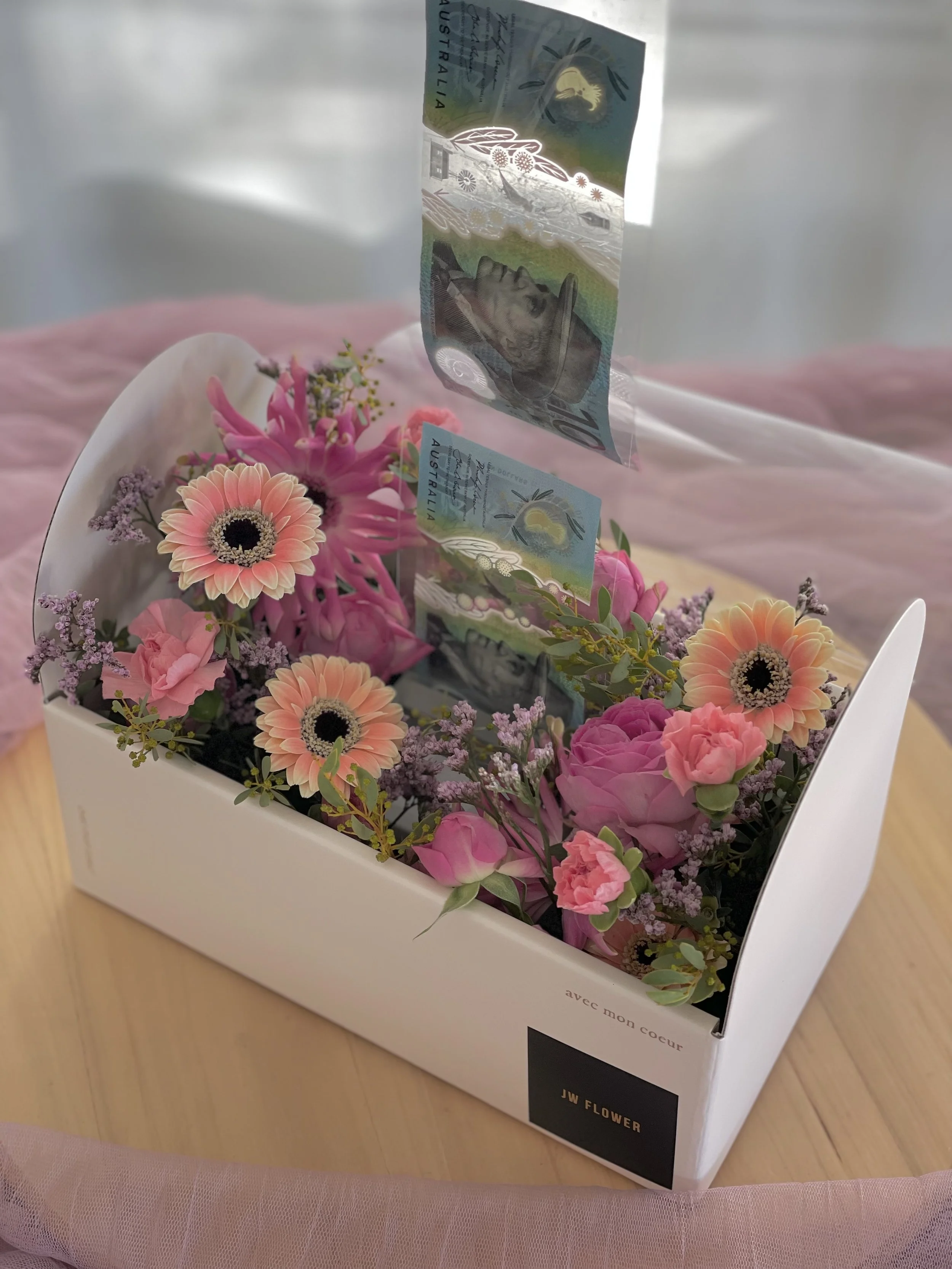A white flower box containing pink and purple flowers with Australian fifty-dollar bills floating above it.