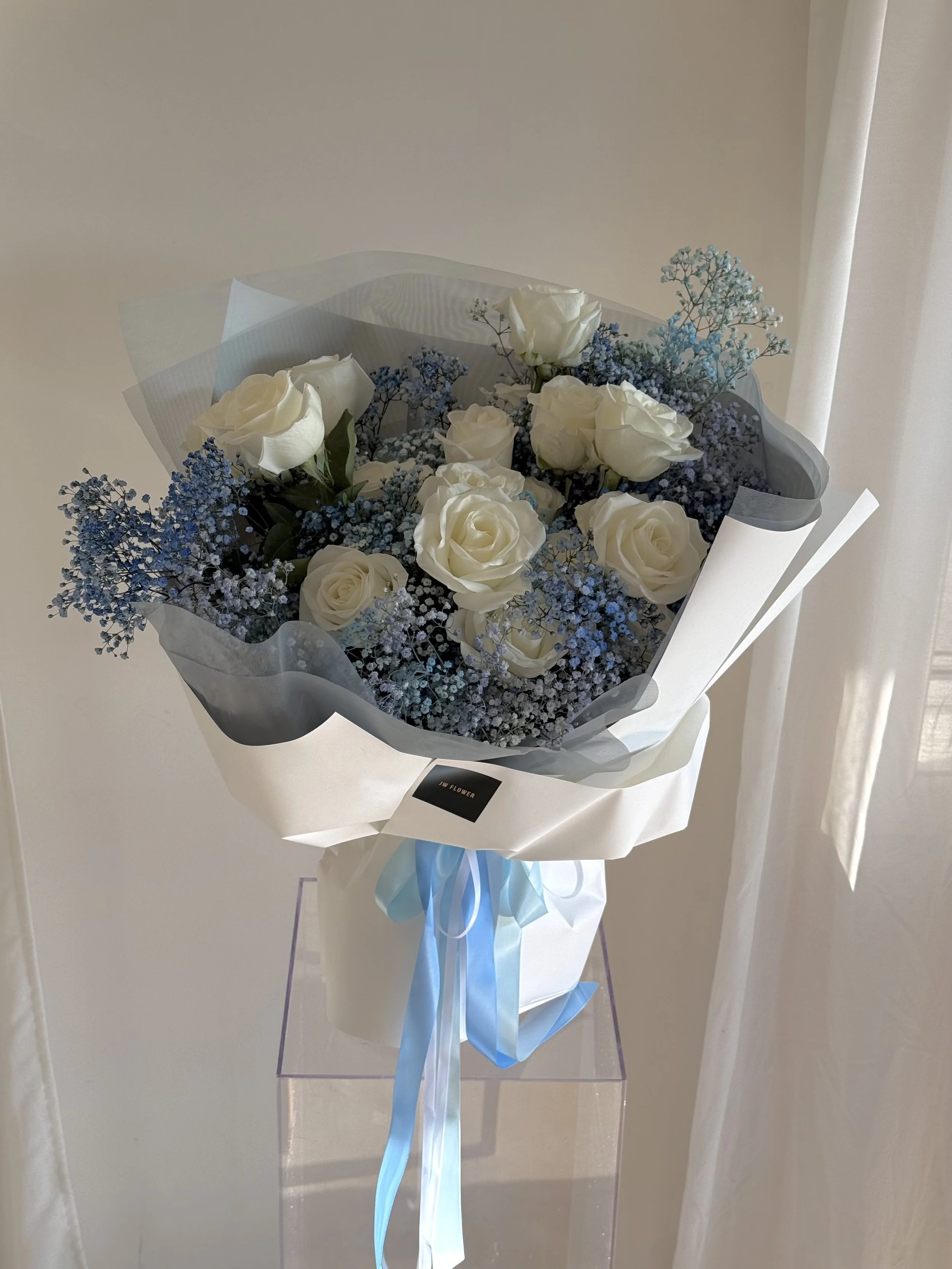 Bouquet of white roses and blue baby's breath flowers wrapped in white and black paper with a blue ribbon