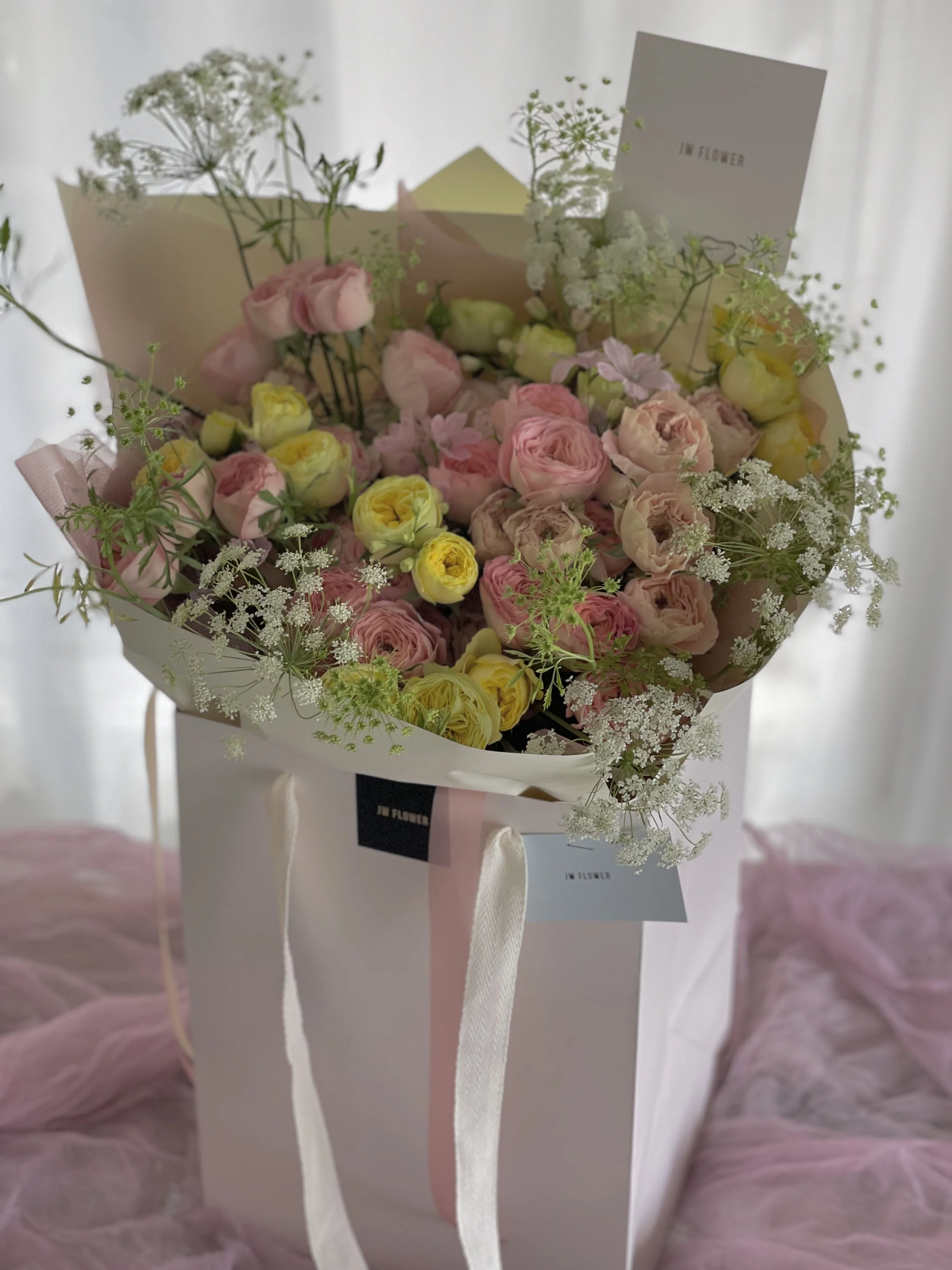 A bouquet of pink and yellow flowers with white filler flowers in a pink and white gift box.