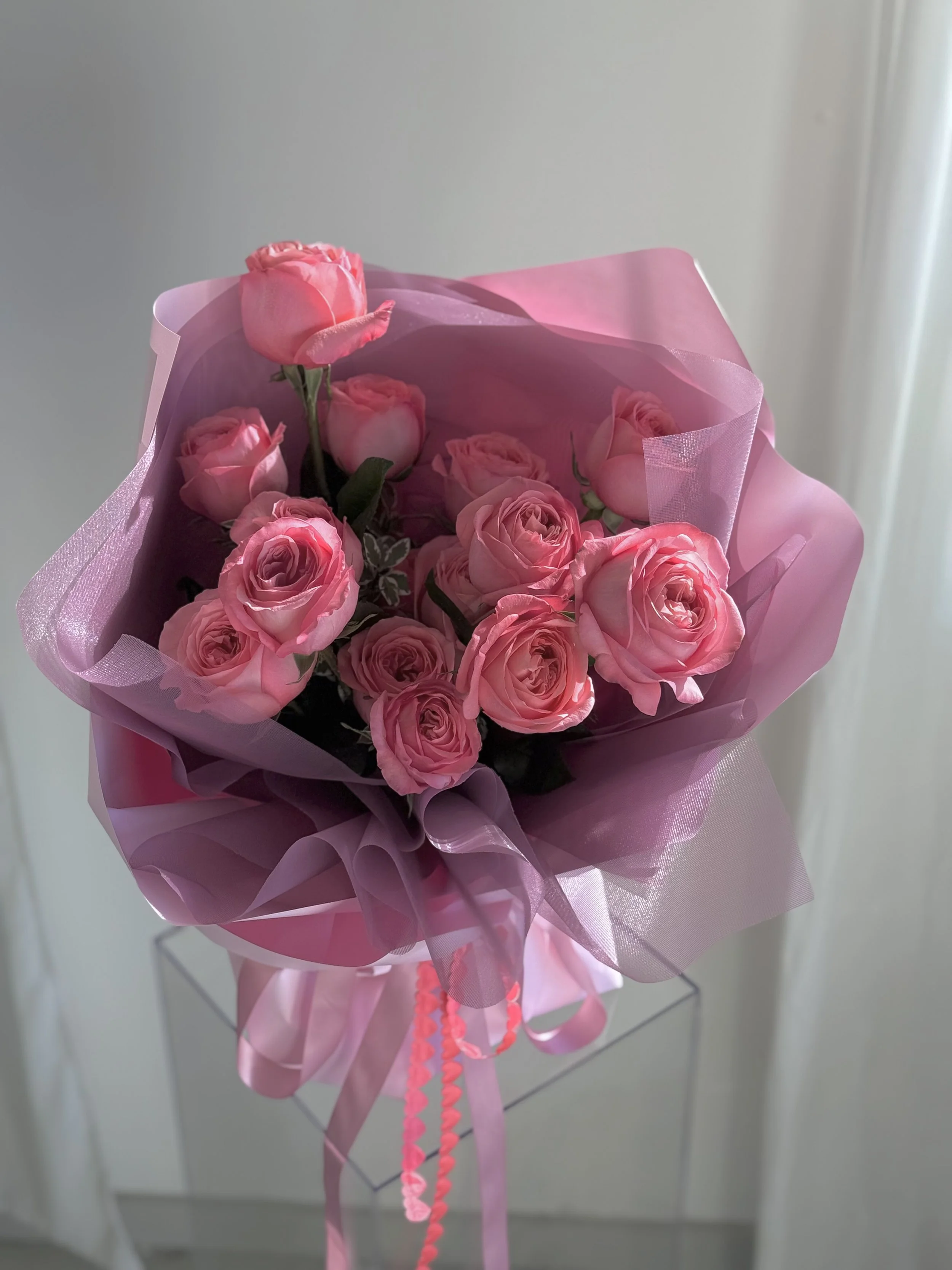 Pink roses bouquet wrapped in pink and purple cellophane with pink ribbons.