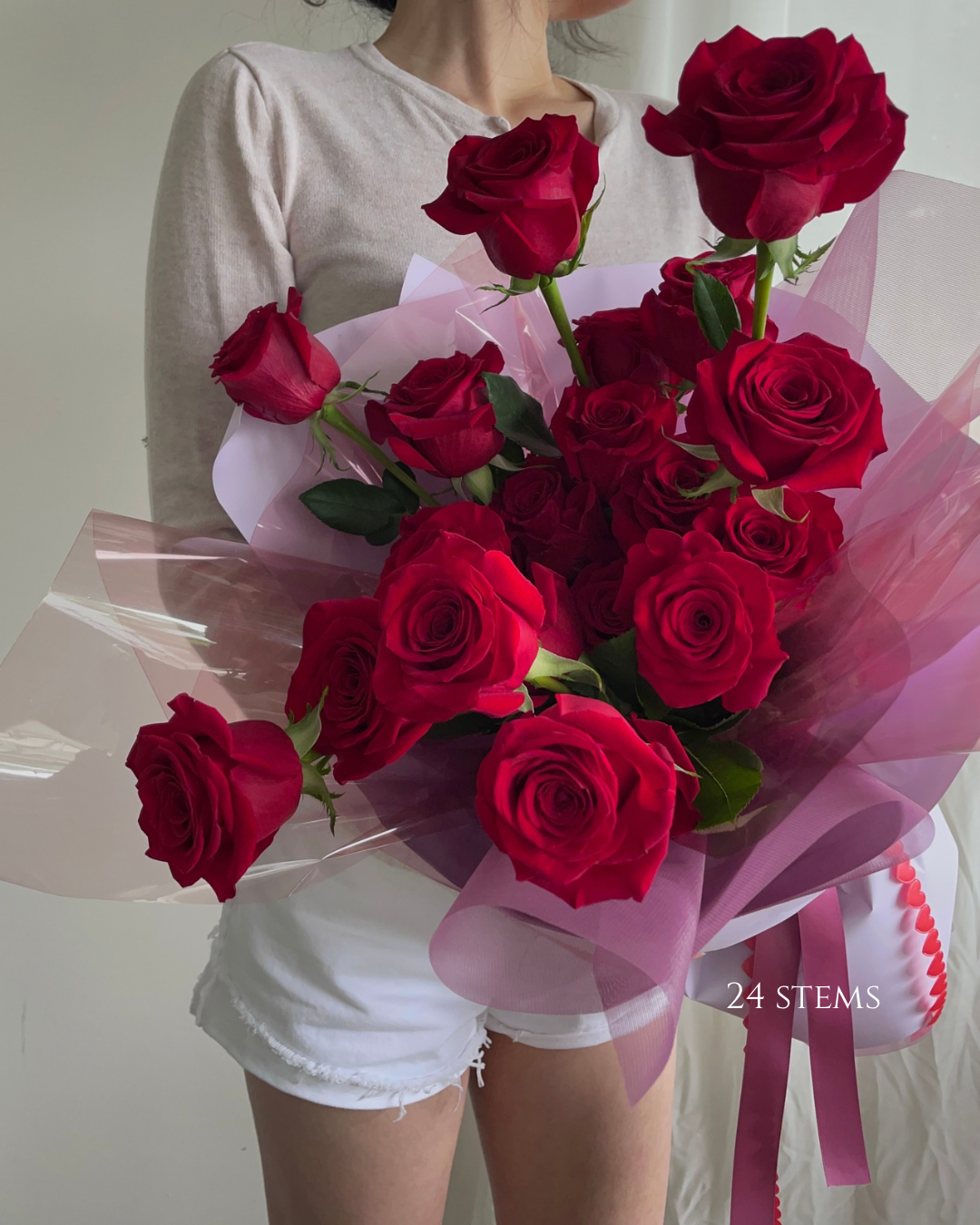 A person holding a large bouquet of 24 red roses wrapped in pink and clear cellophane with a pink ribbon.
