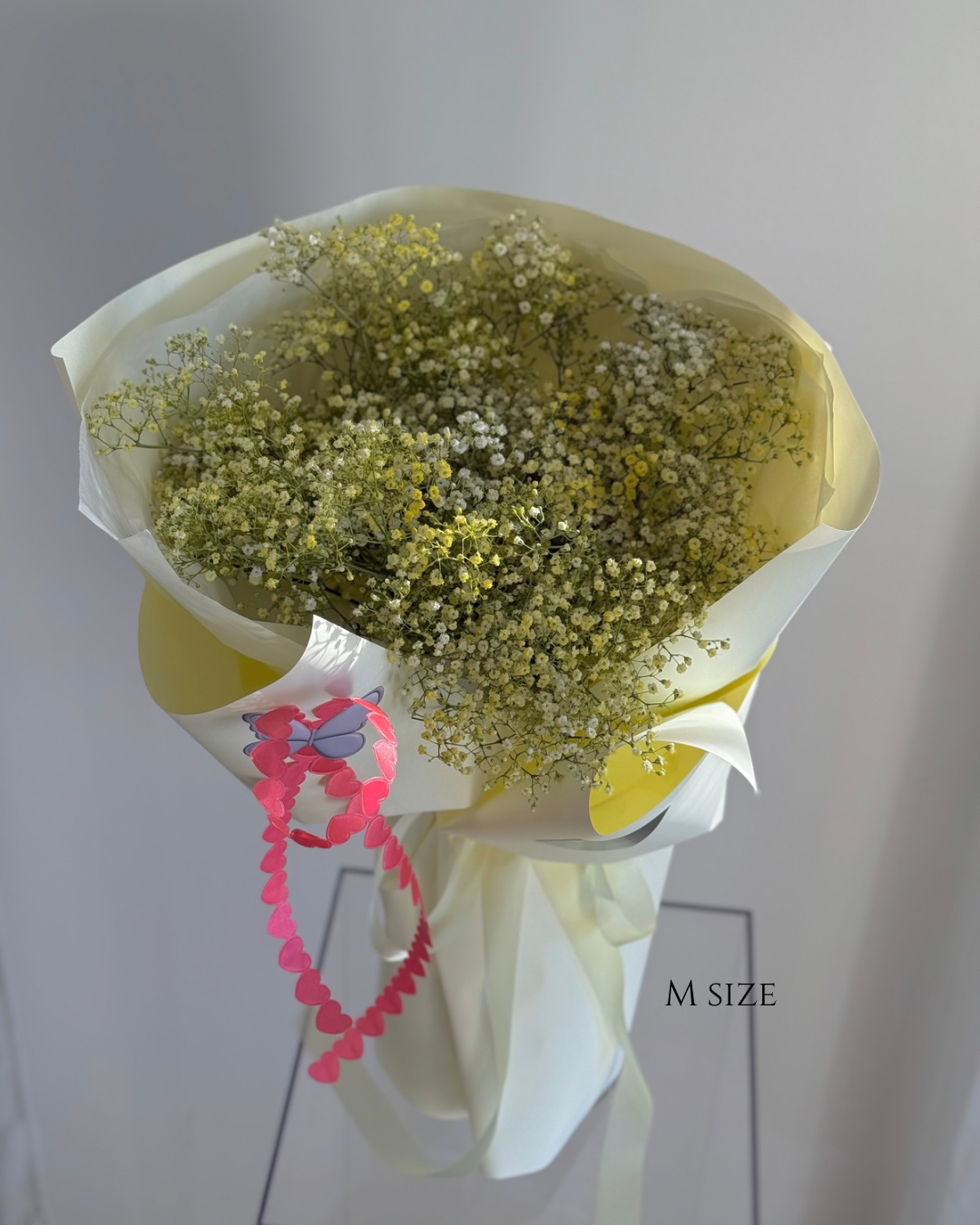 Small bouquet of baby's breath flowers wrapped in white and yellow paper with a pink heart-shaped decoration attached.