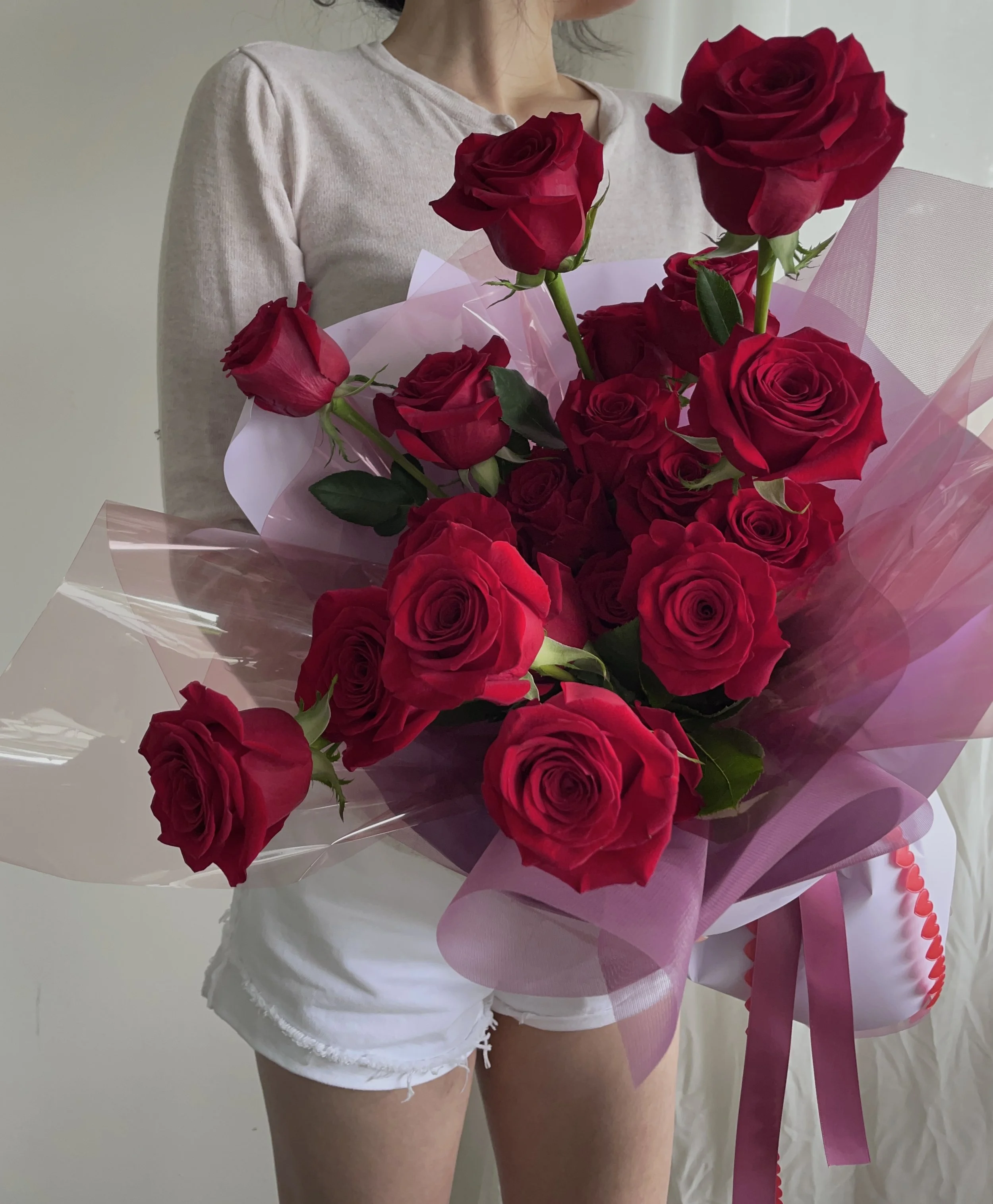 Person holding a large bouquet of red roses wrapped in pink and clear wrapping paper.