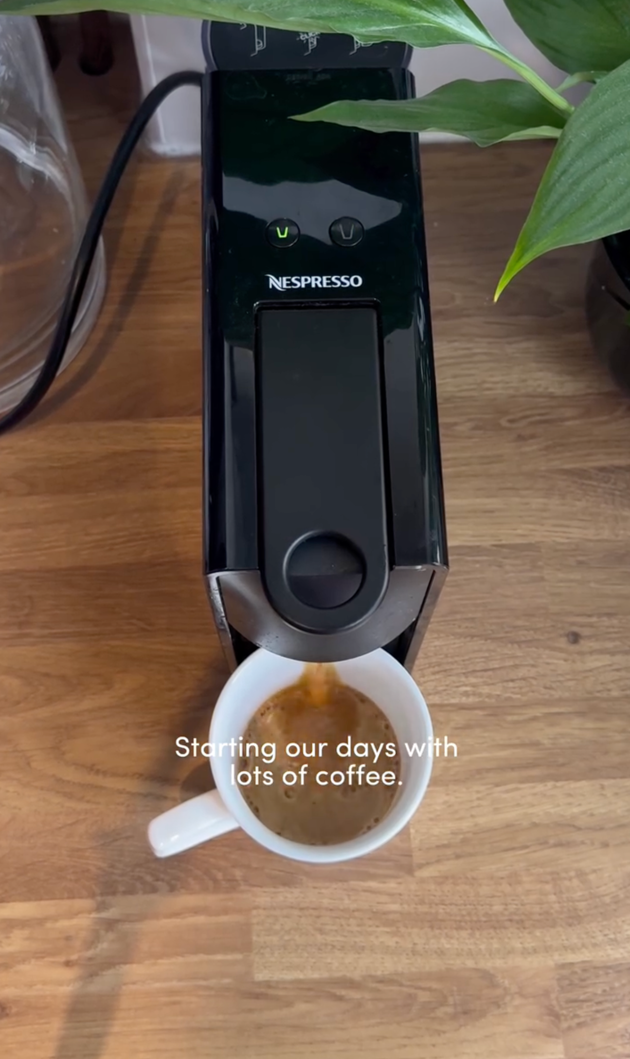 A Nespresso coffee machine brewing coffee into a white mug on a wooden surface, with plants nearby and a caption that reads 'Starting our days with lots of coffee.'