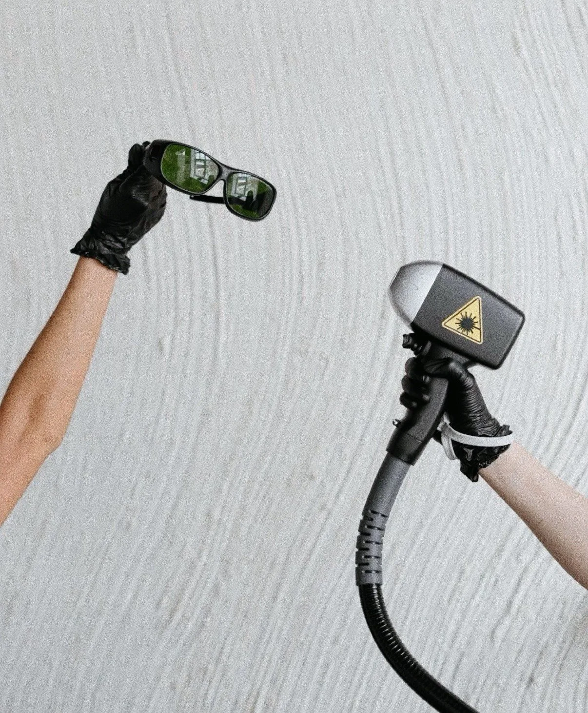 Kaksi ihmistä käyttävät käsitaitteita, yksi kädessä on suojakäsine ja toinen on säteilymittari tai laserinstrumentti, joka varoittaa vaarasta.