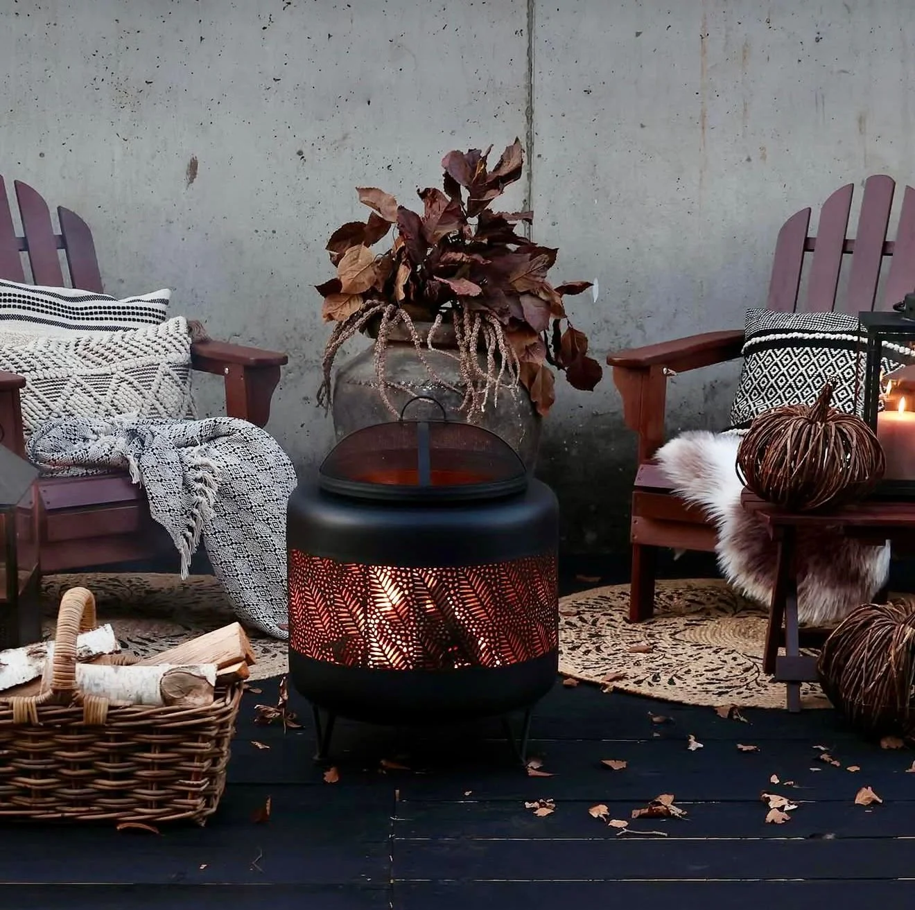 Gemütliche Sitzecke mit zwei Holzstühlen, einer Decke, einer Fußbodenheizung, einem Korb mit Brennholz, Herbstdekoration und Kerzen auf einem Außenbereich mit dunklem Holzboden.