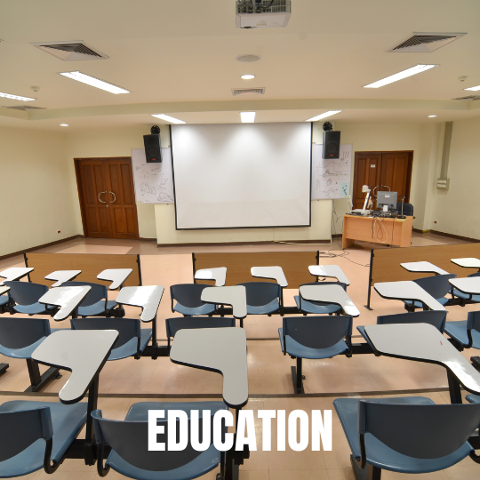 Empty classroom with rows of blue chairs and desks facing a large white projection screen. The setting is orderly, with a focus on "Education."