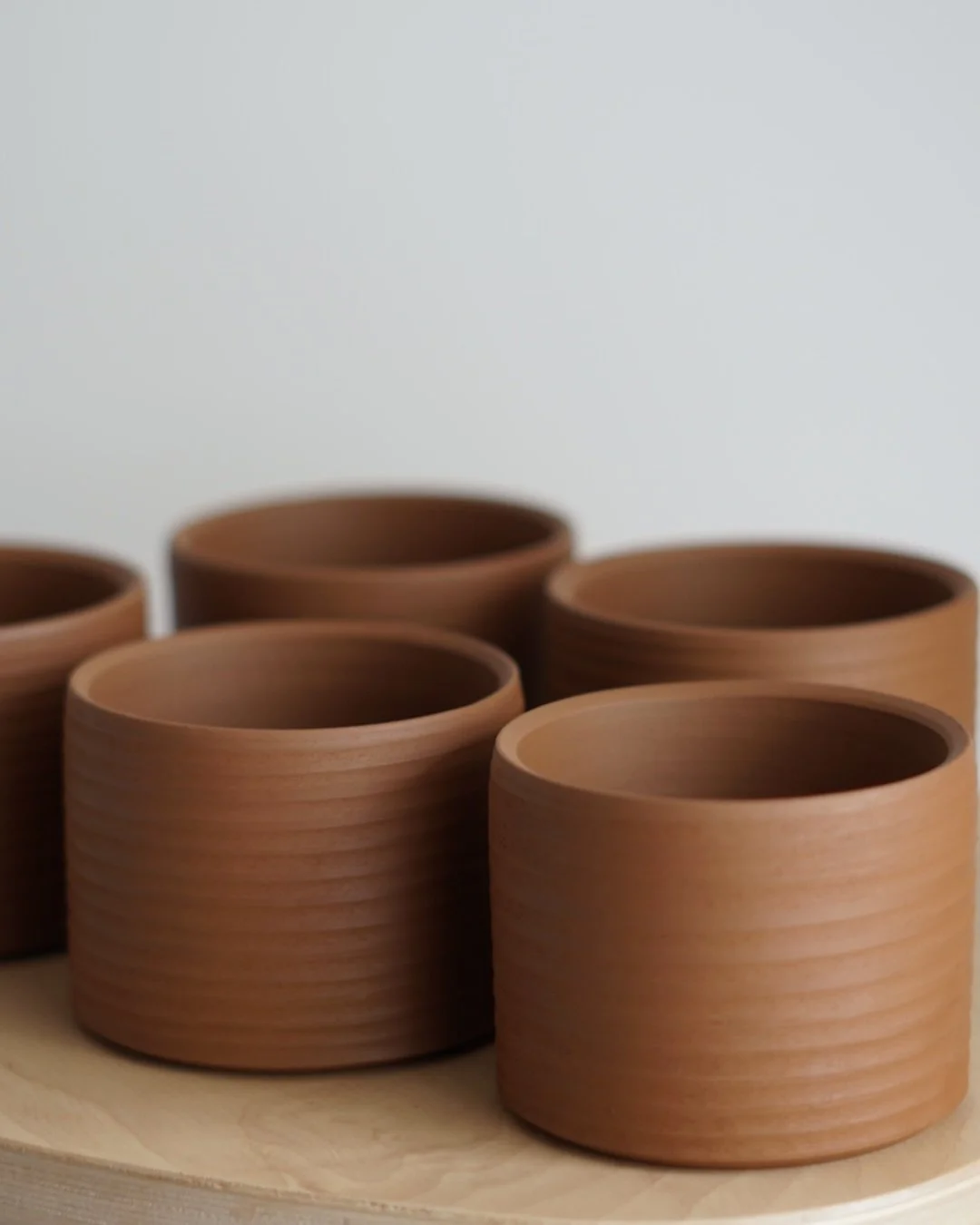 Six empty brown ceramic cups arranged on a wooden surface against a plain light background.