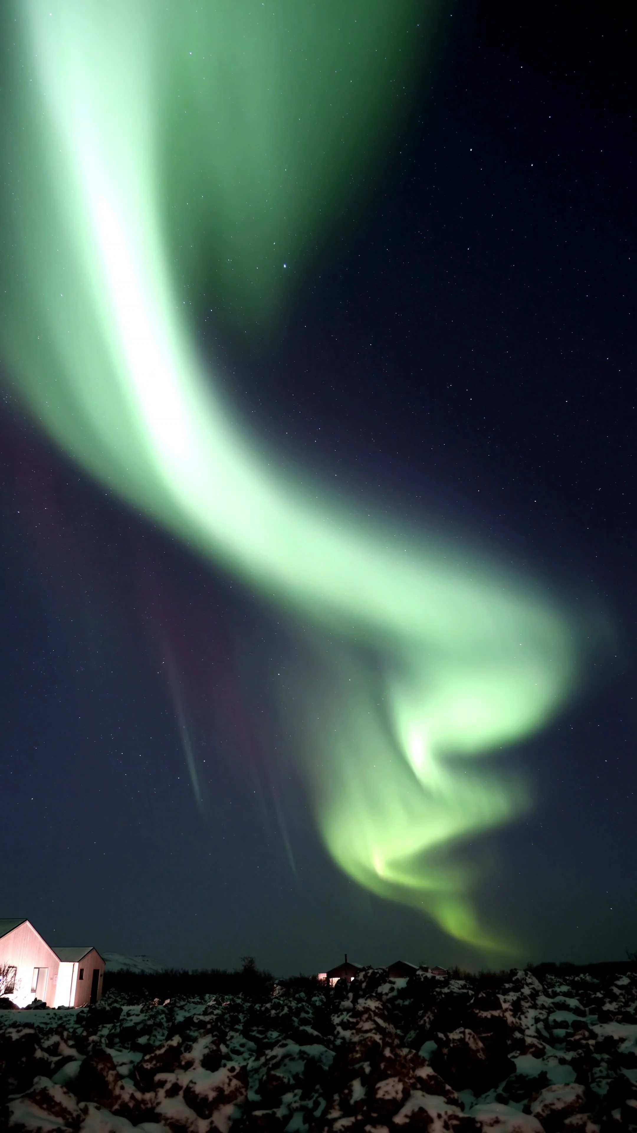 Northern lights in the night sky over snowy landscape with small buildings.