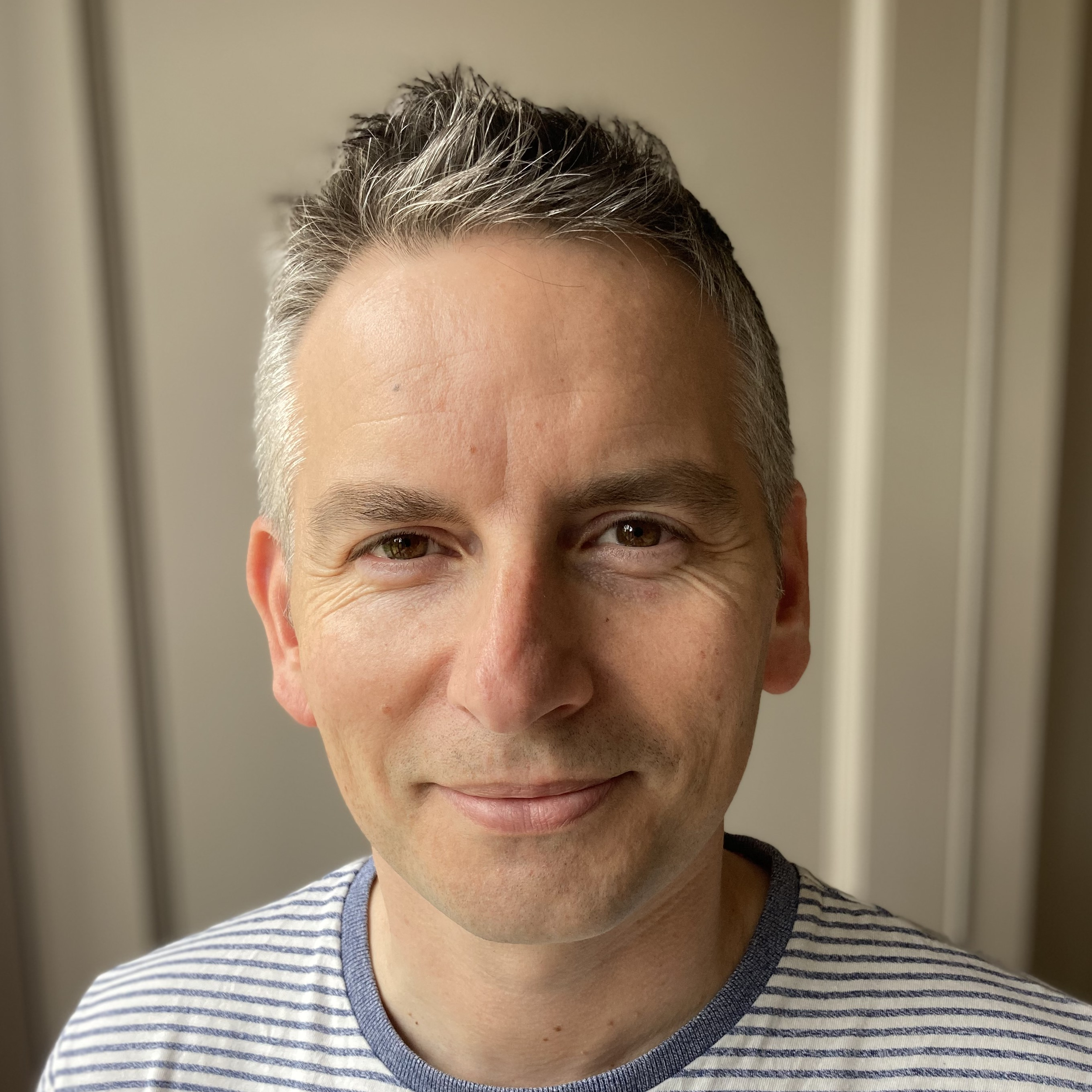 Close-up portrait of Rich Allen with short, graying hair, smiling slightly with one eye closed, wearing a striped shirt.