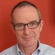 A man with glasses and short hair, wearing a collared shirt, positioned against a red background.