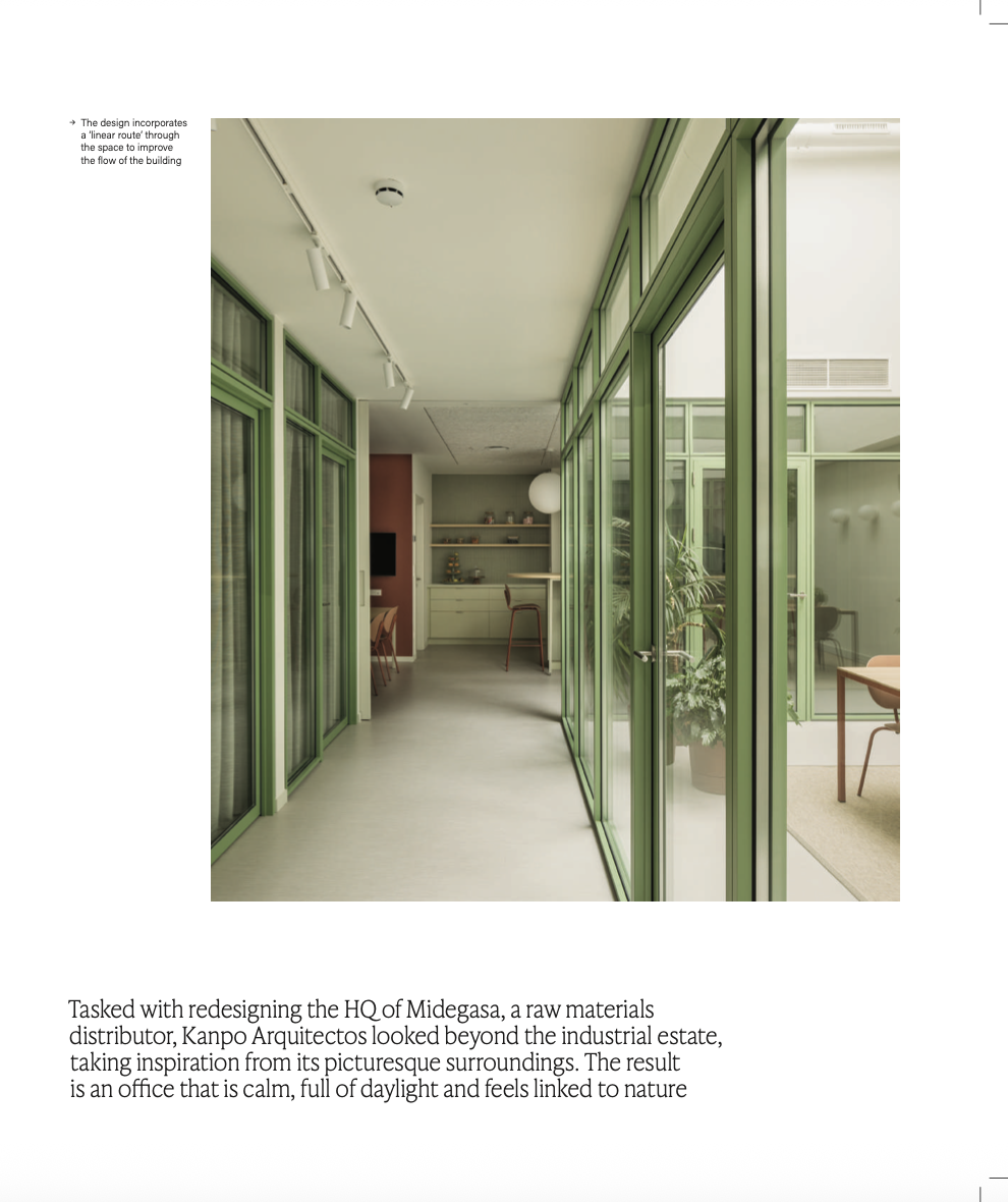 Pasillo con paredes de cristales con marco verde y vista hacia interiores con plantas y muebles.