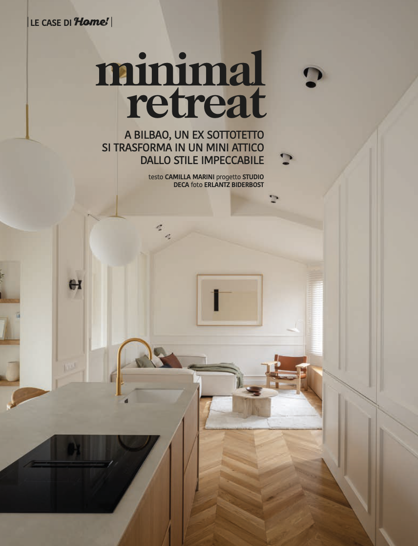 Interior de sala minimalista con muebles blancos y madera, sillón grande, mesa de centro, lámparas colgantes y paredes decoradas con arte.