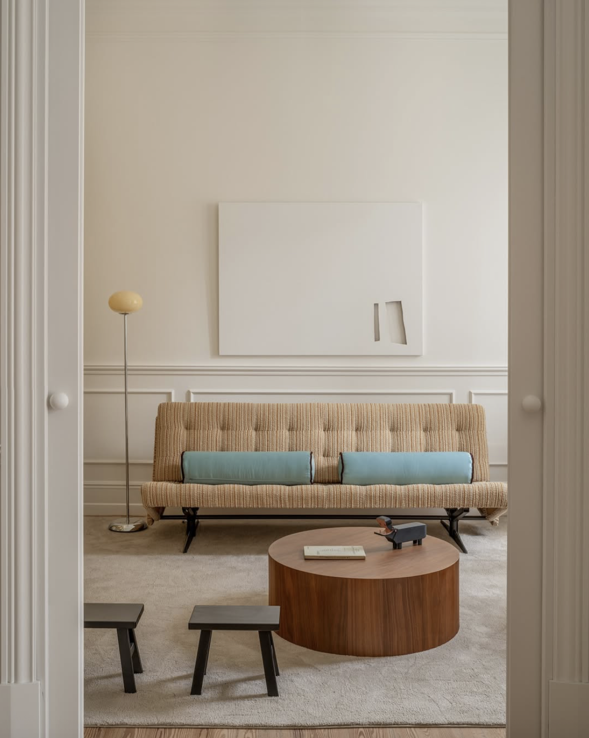 Sala de estar con sillón de línea recta, mesa de centro de madera, un libro y una figura decorativa en forma de animal. Hay una lámpara de pie y un cuadro abstracto en la pared.