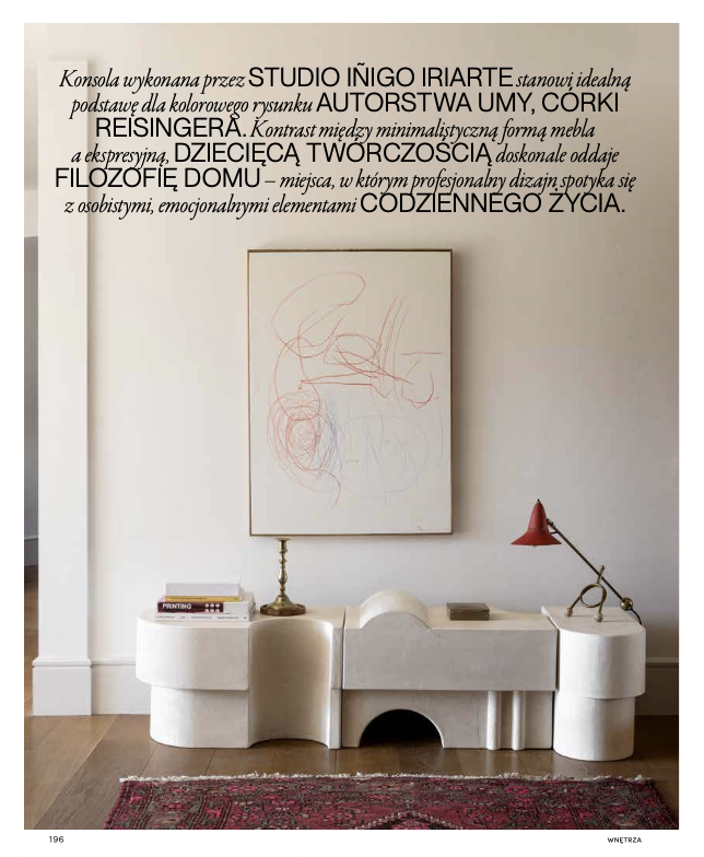 Decoración moderna en una sala con una obra de arte abstracto en la pared, una consola blanca con libros y decoración, y una lámpara roja