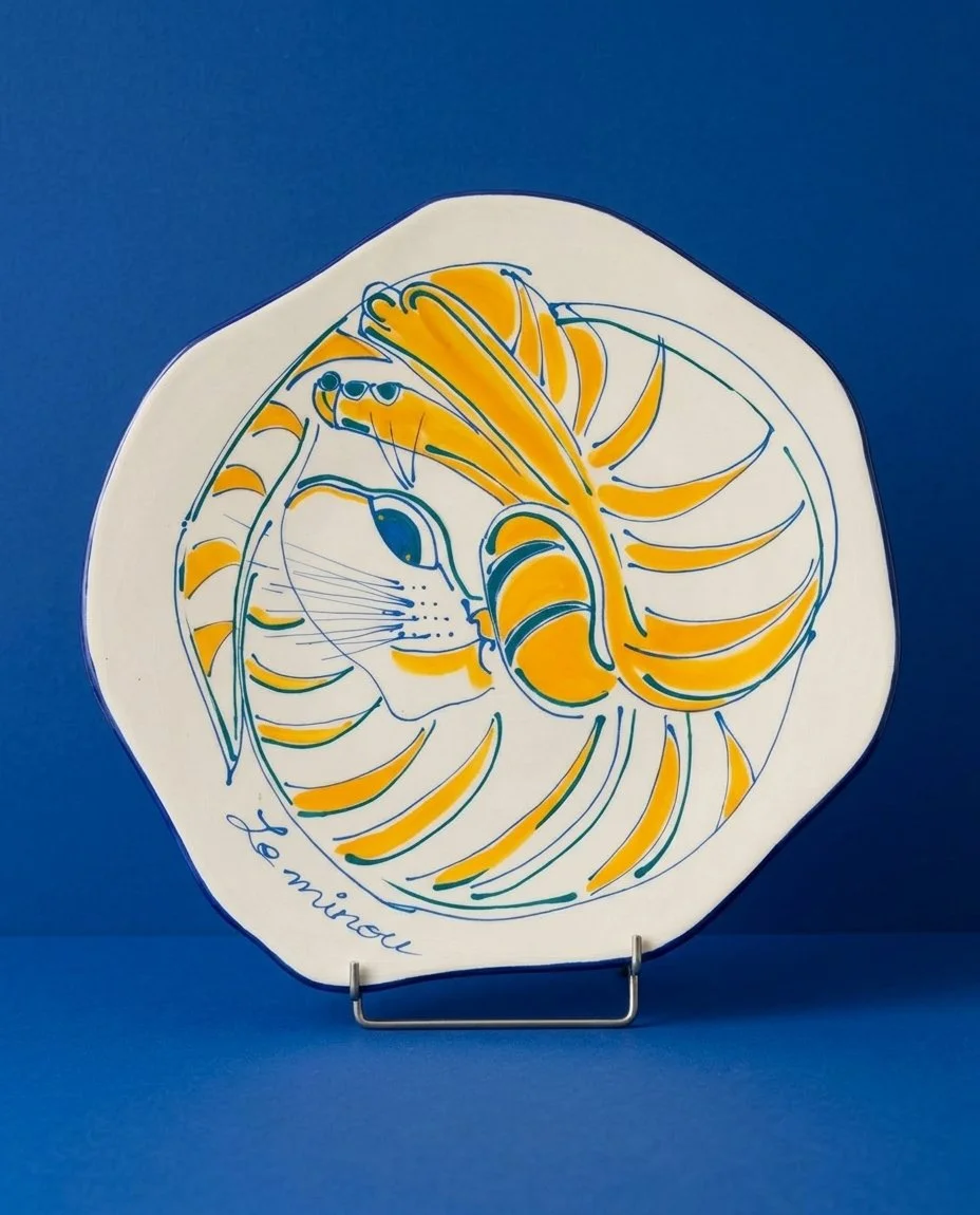 Assiette en céramique avec un dessin stylisé d'une moufle mélangée à une queue de poisson, avec le texte "Le minou" en bas.