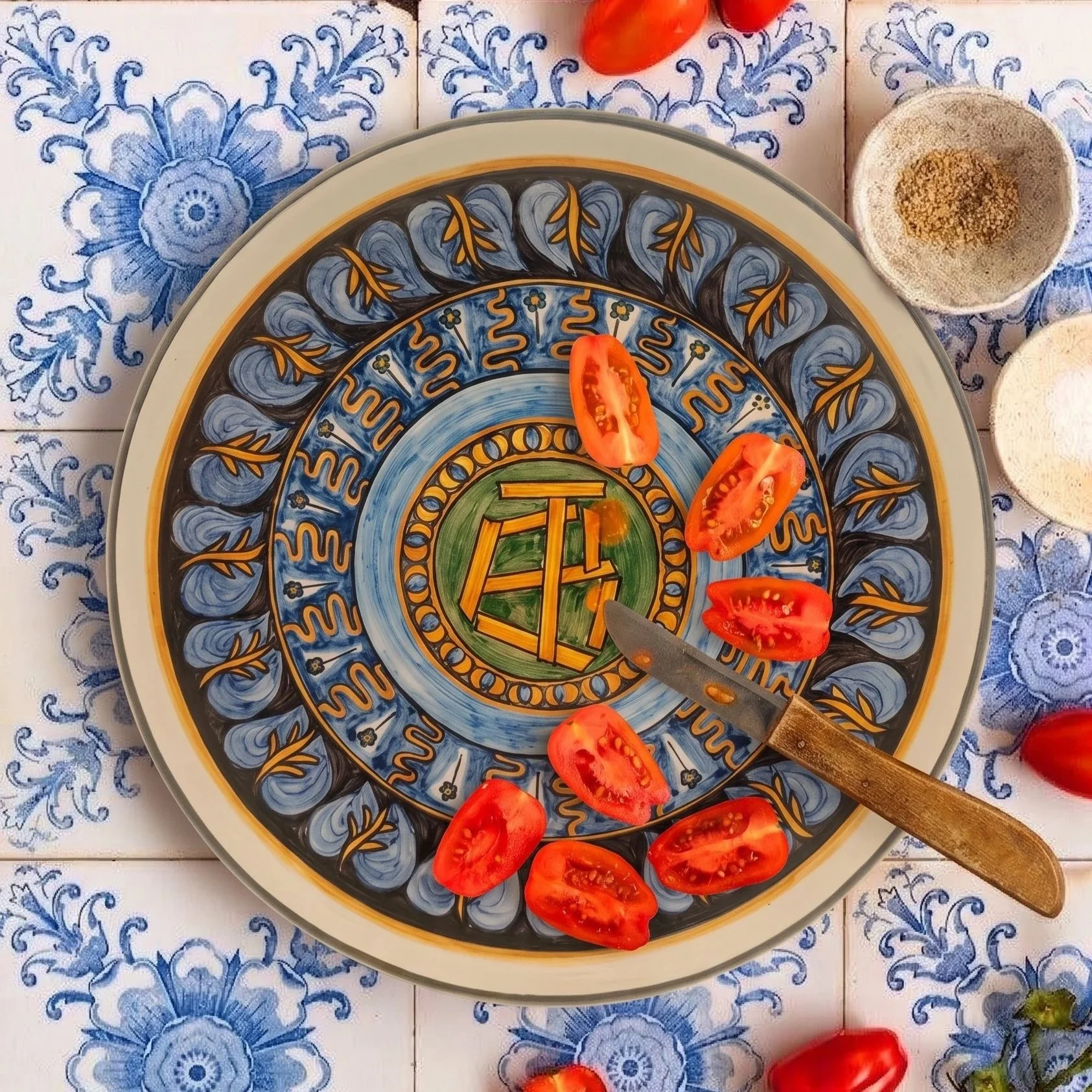 Assiette avec des tranches de tomate, une petite cuillère, et un décor de vaisselle en céramique bleue et jaune. La table est recouverte d'une nappe aux motifs bleus.
