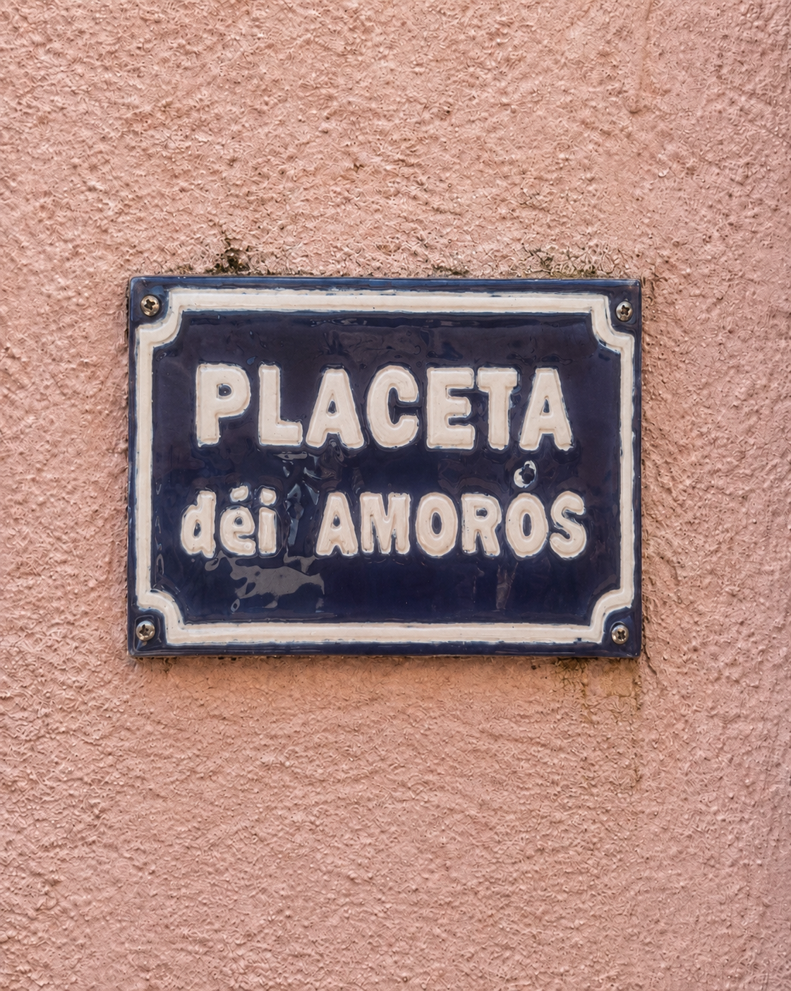 Plaque de rue bleue avec l'inscription 'Placeta dei Amoros' fixée sur un mur rose.