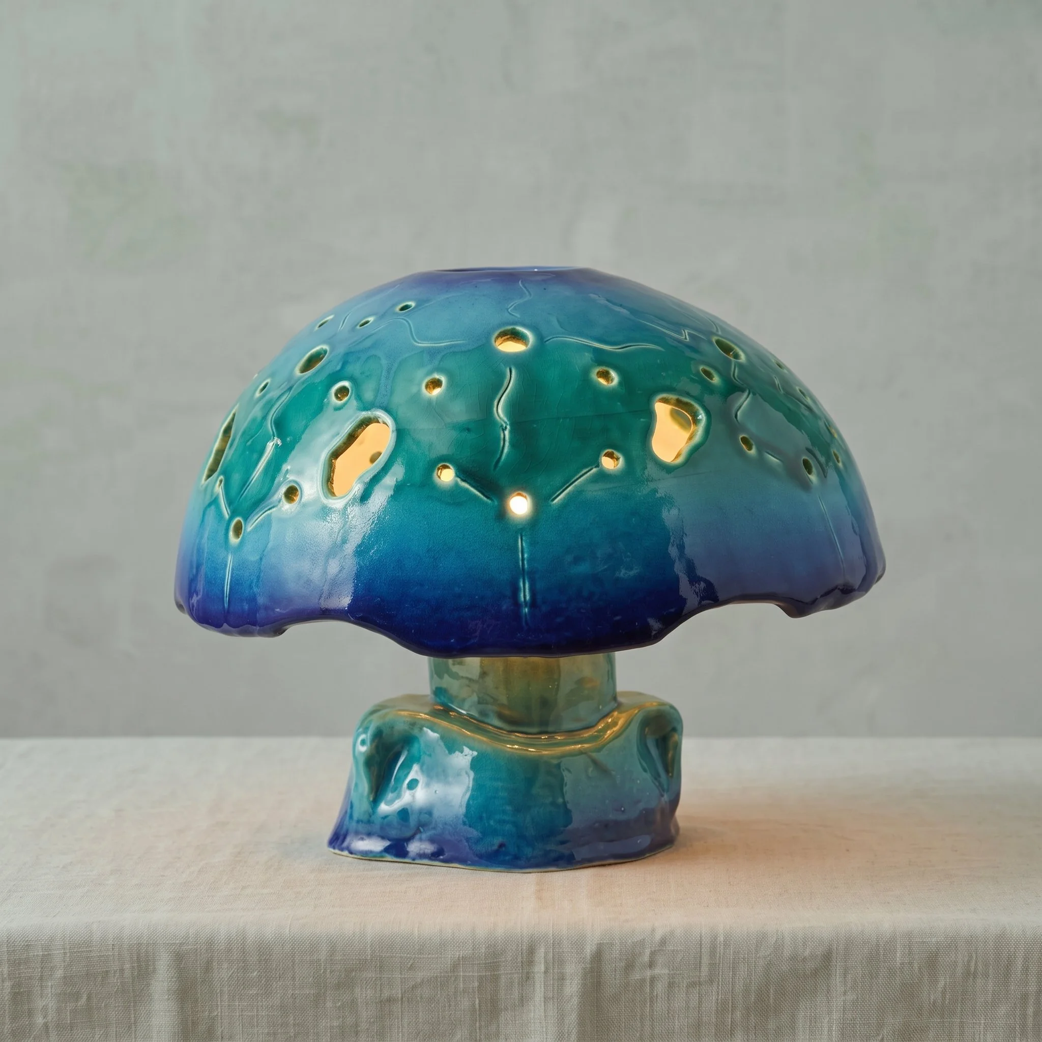 Une lampe ou une sculpture en verre coloré avec des motifs perforés, dans des tons de bleu et vert, placée sur une surface plane.