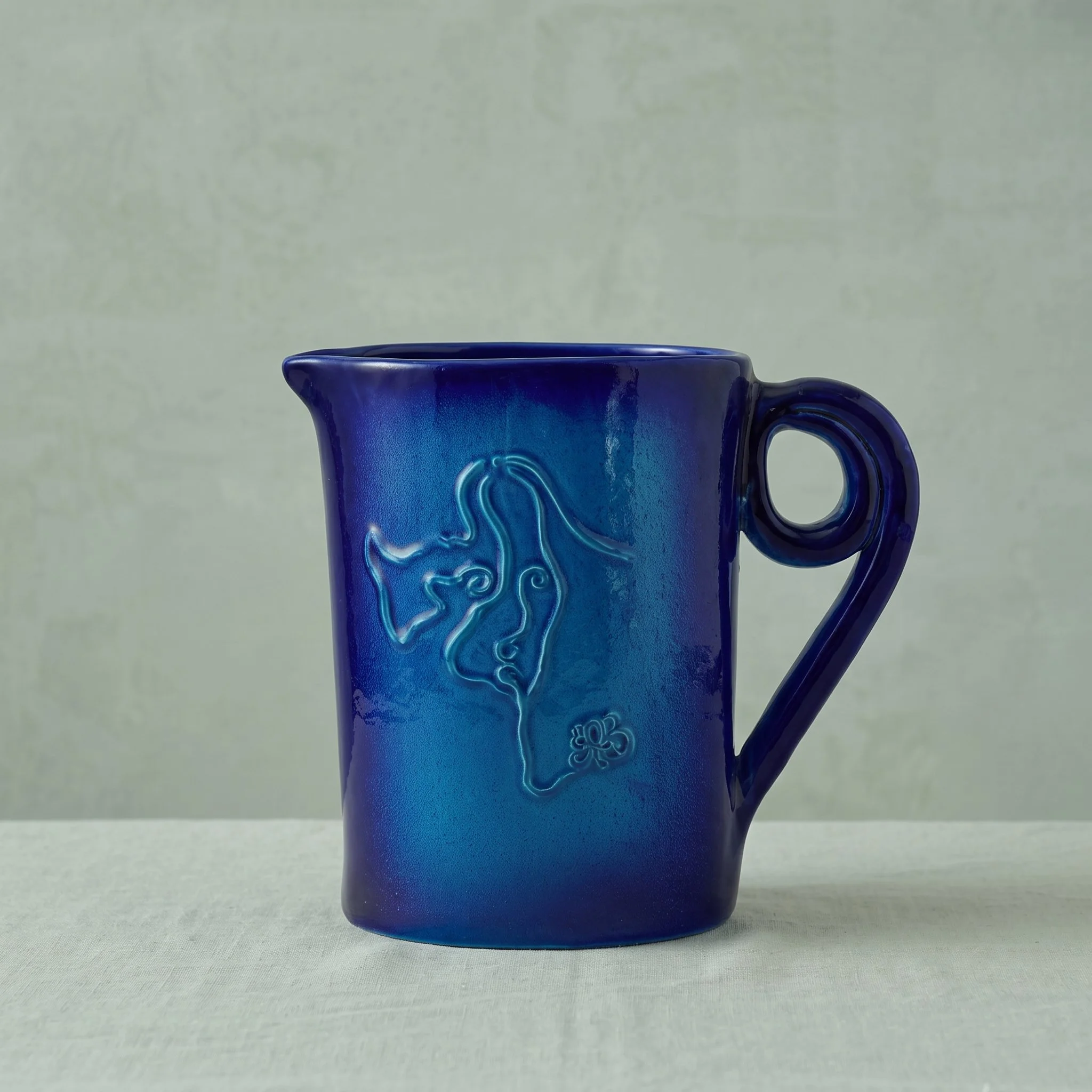 Une tasse en céramique bleu foncé avec un design gravé sur sa surface, placée sur une surface plane contre un fond neutre.