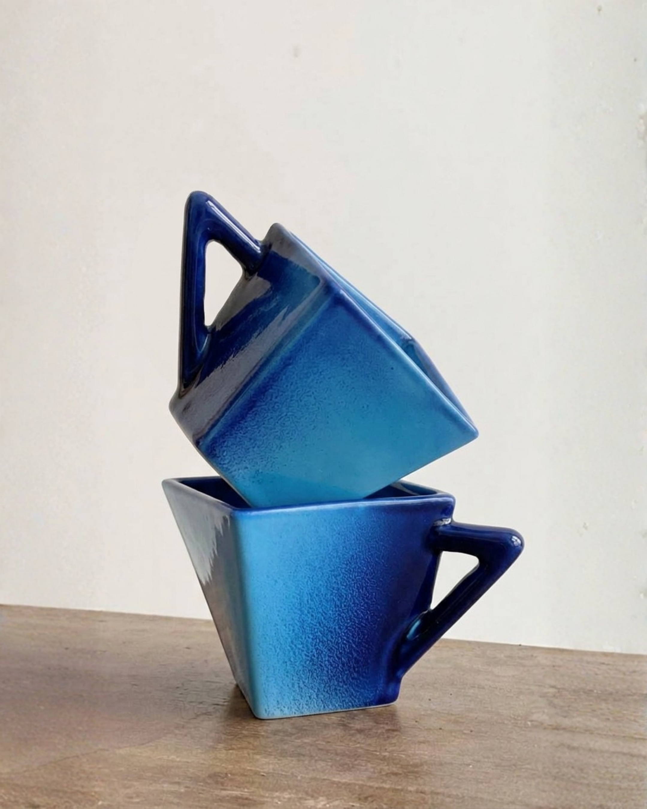 Une collection de petits contenants en céramique de différentes nuances de bleu, empilés de manière artistique sur une surface en bois, avec un fond blanc.