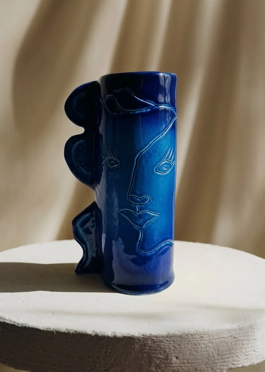 Vase bleu en céramique avec une illustration de visage stylisé en lignes simples.