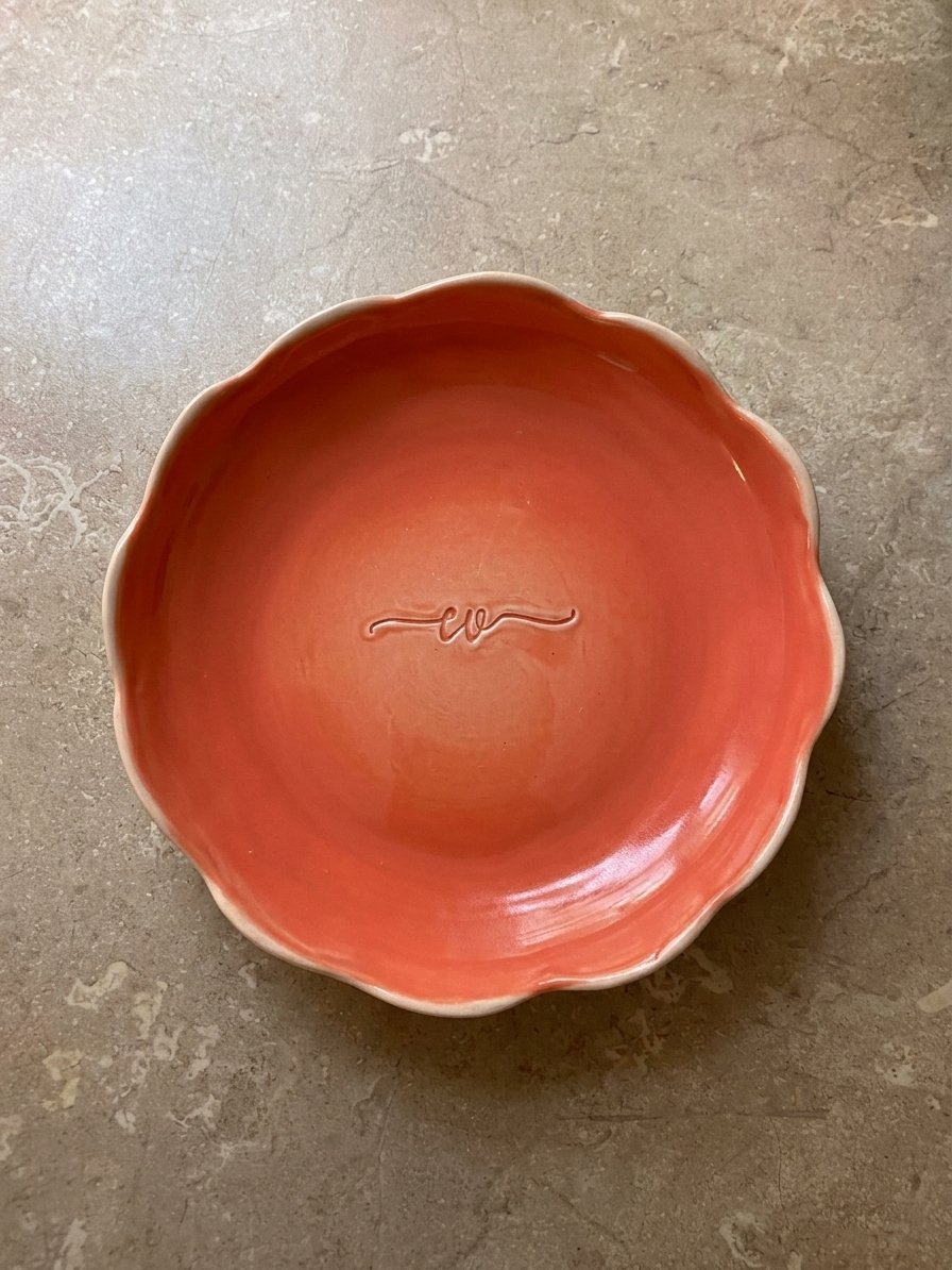 Bol en céramique de couleur orange avec une forme ondulée, posé sur une surface en pierre
