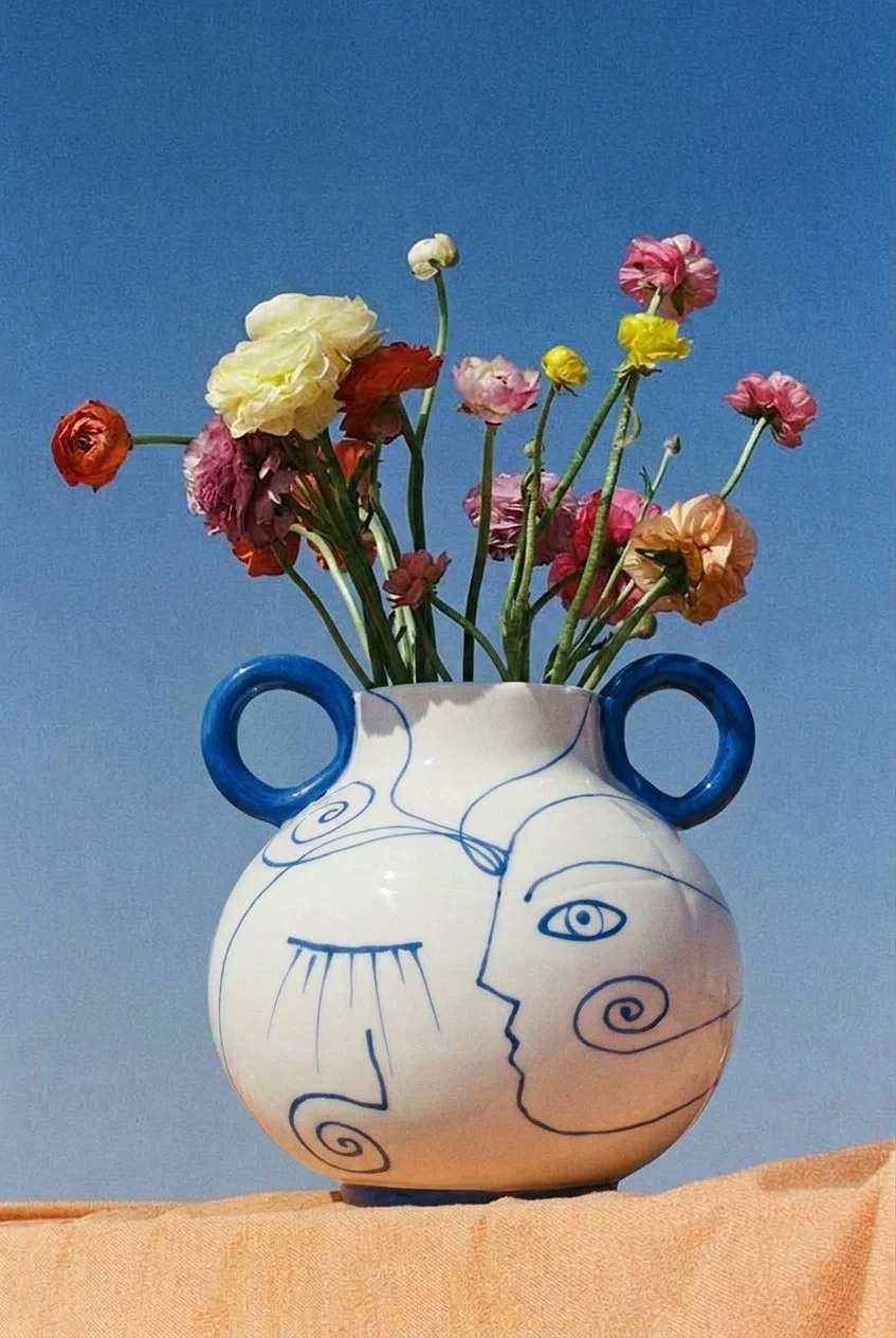 Vase blanc avec des dessins abstraits en bleu, contenant des fleurs colorées, sur fond de ciel bleu
