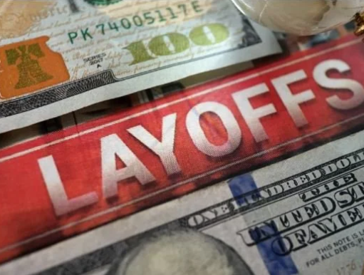Close-up of cash and a red sign with the word 'LAYOFFS' in white letters.